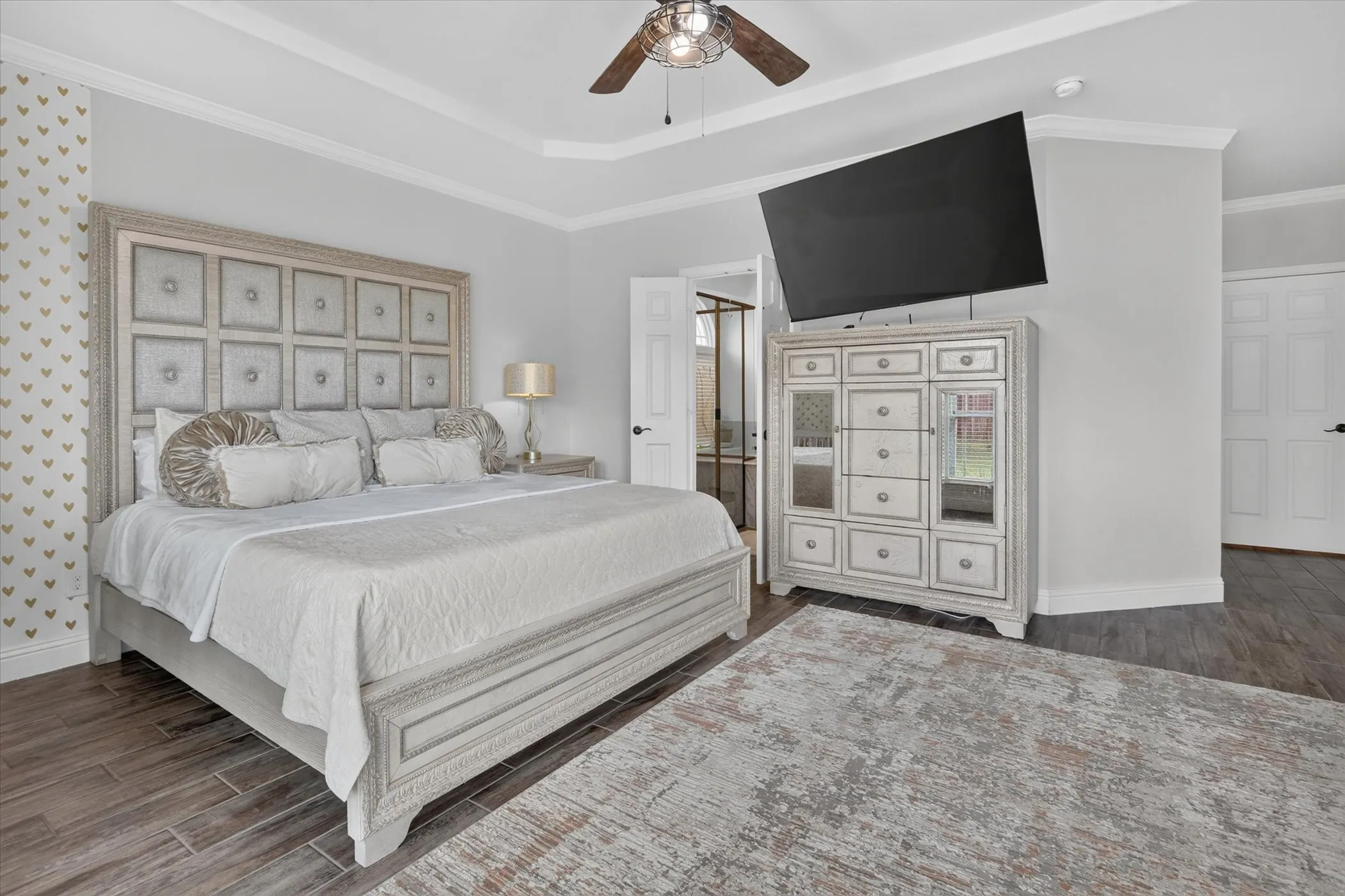 Tray ceiling with crown molding, wood-finish flooring, and built-in wall-mounted television