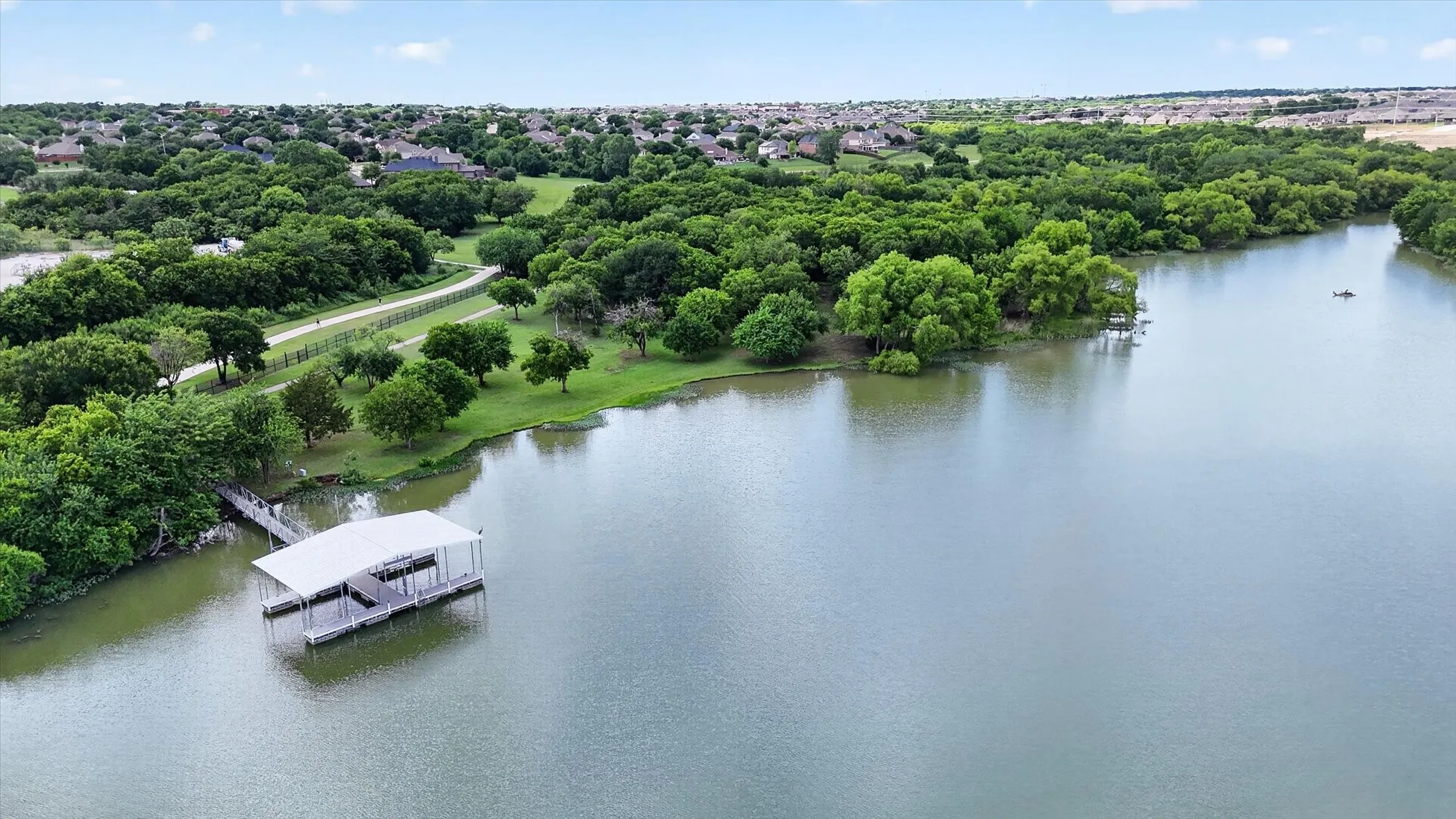 Waterfront property featuring a private boat dock with covered slip, lush green landscaping, and a meandering paved pathway along the shoreline