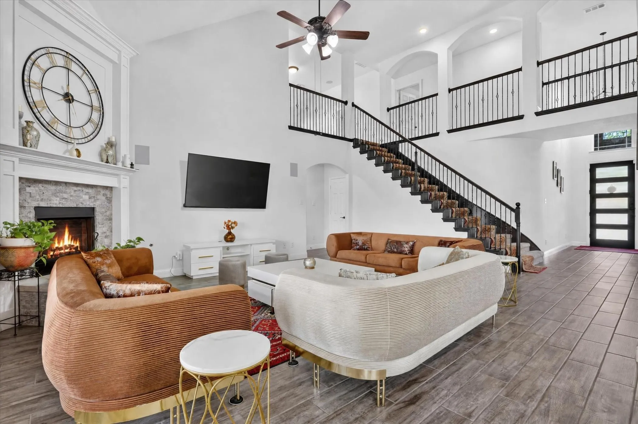 Spacious living area featuring a vaulted ceiling, a fireplace with a stone surround, and wood-finish flooring