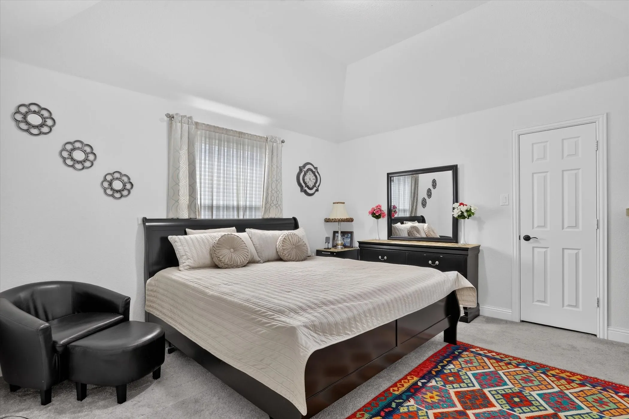 Vaulted ceiling, paneled interior door, window with curtains, carpet flooring, and a mirrored dresser