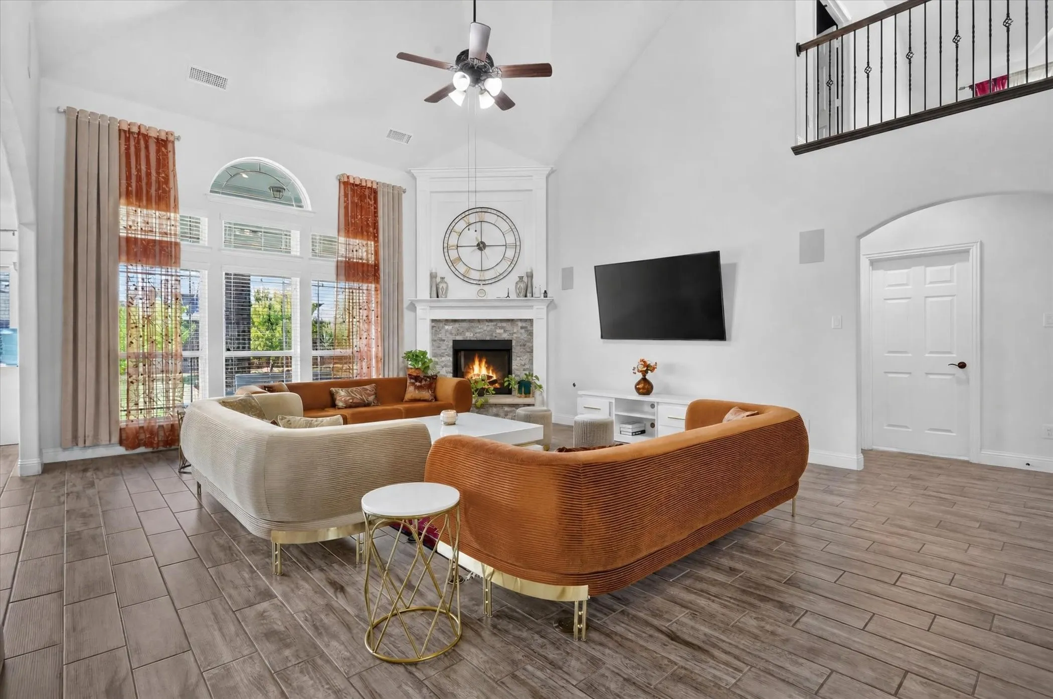 Vaulted ceilings with a ceiling fan, wood-finish flooring, a stone-surround fireplace with a mantel, and an arched doorway