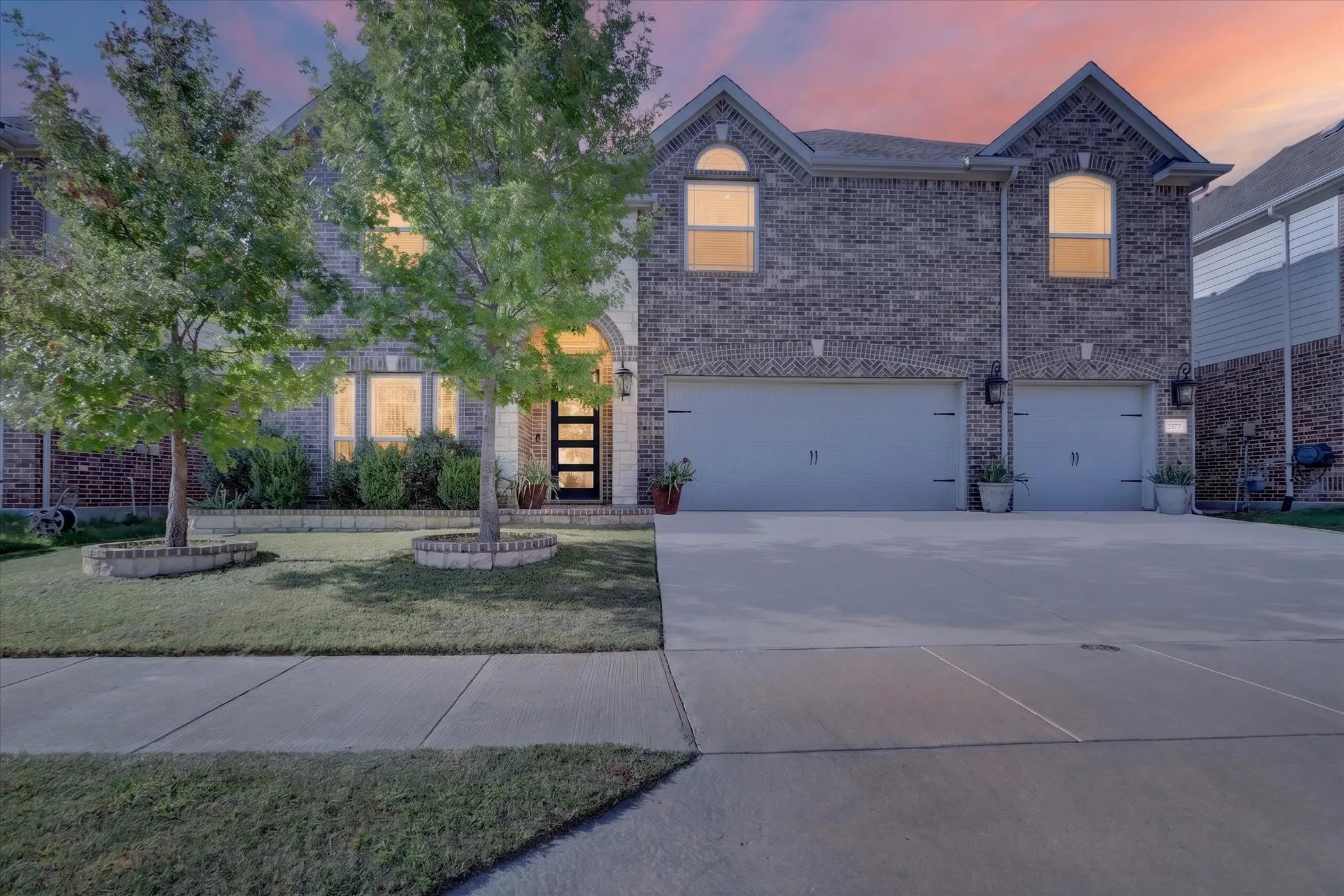 Brick facade, arched entry, contemporary front door with frosted glass, dual garage doors, paved driveway