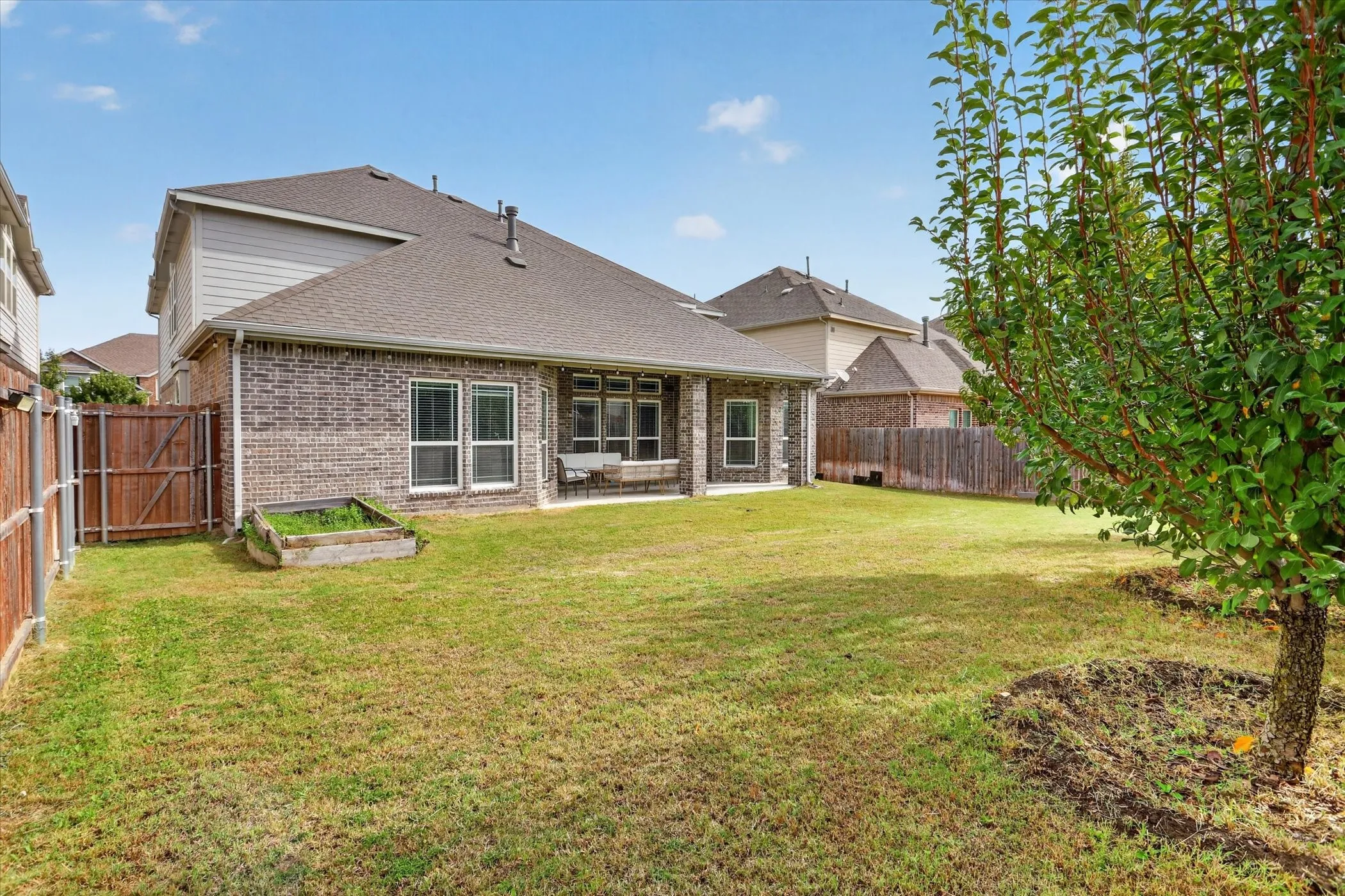 Expansive backyard with a manicured lawn, full privacy fencing, and a raised garden bed
