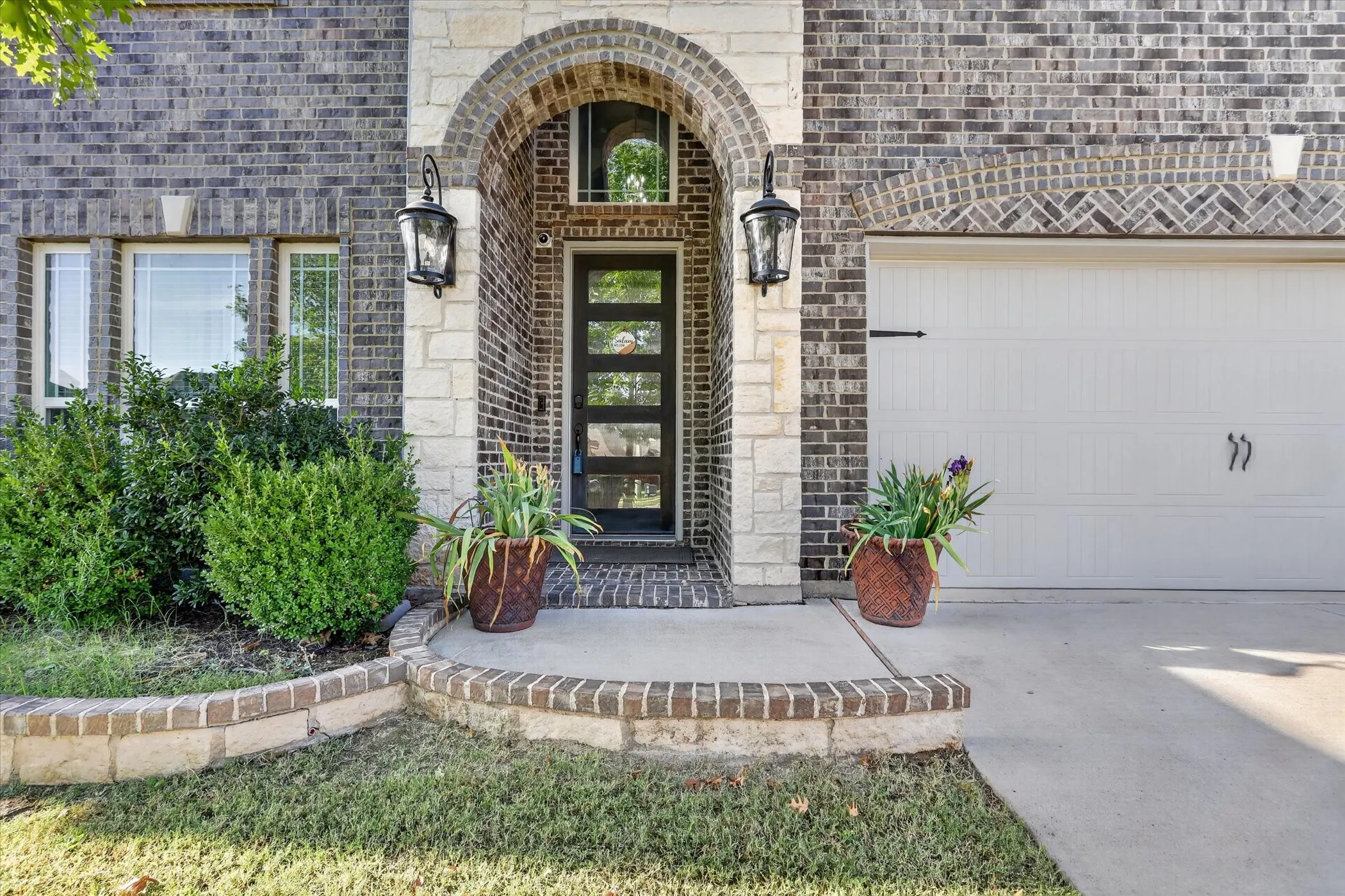 Brick exterior with stone accents, arched entryway, modern glass-panel front door, and a two-car garage with decorative hardware