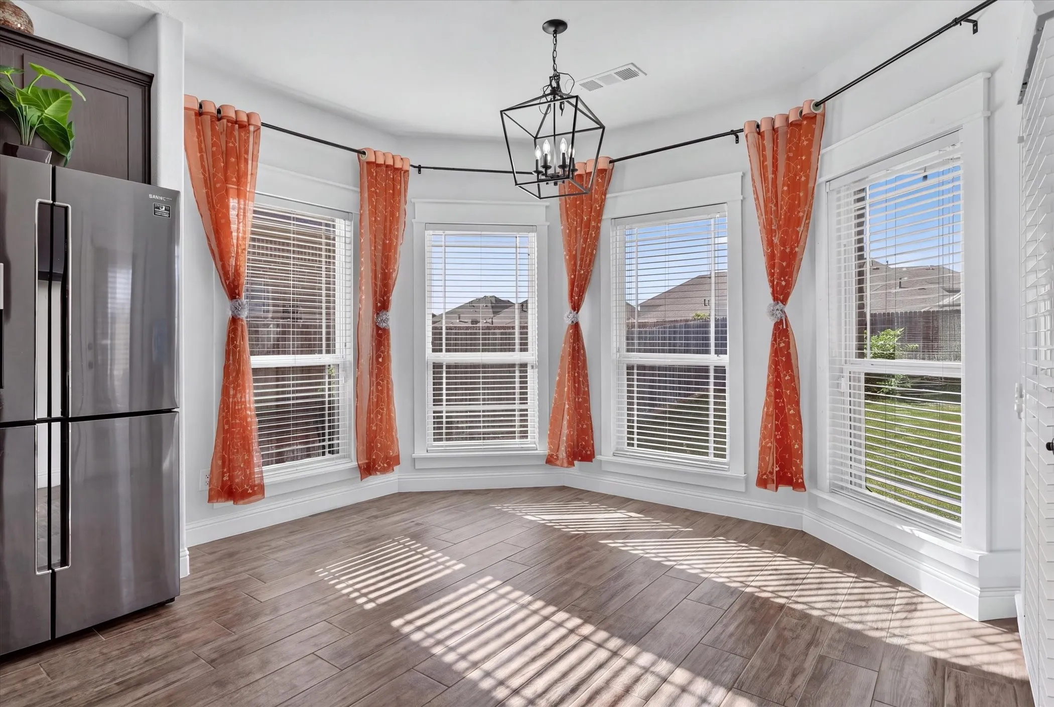 Bay window with multiple large windows, wood-finish flooring, a contemporary chandelier, and a stainless steel refrigerator