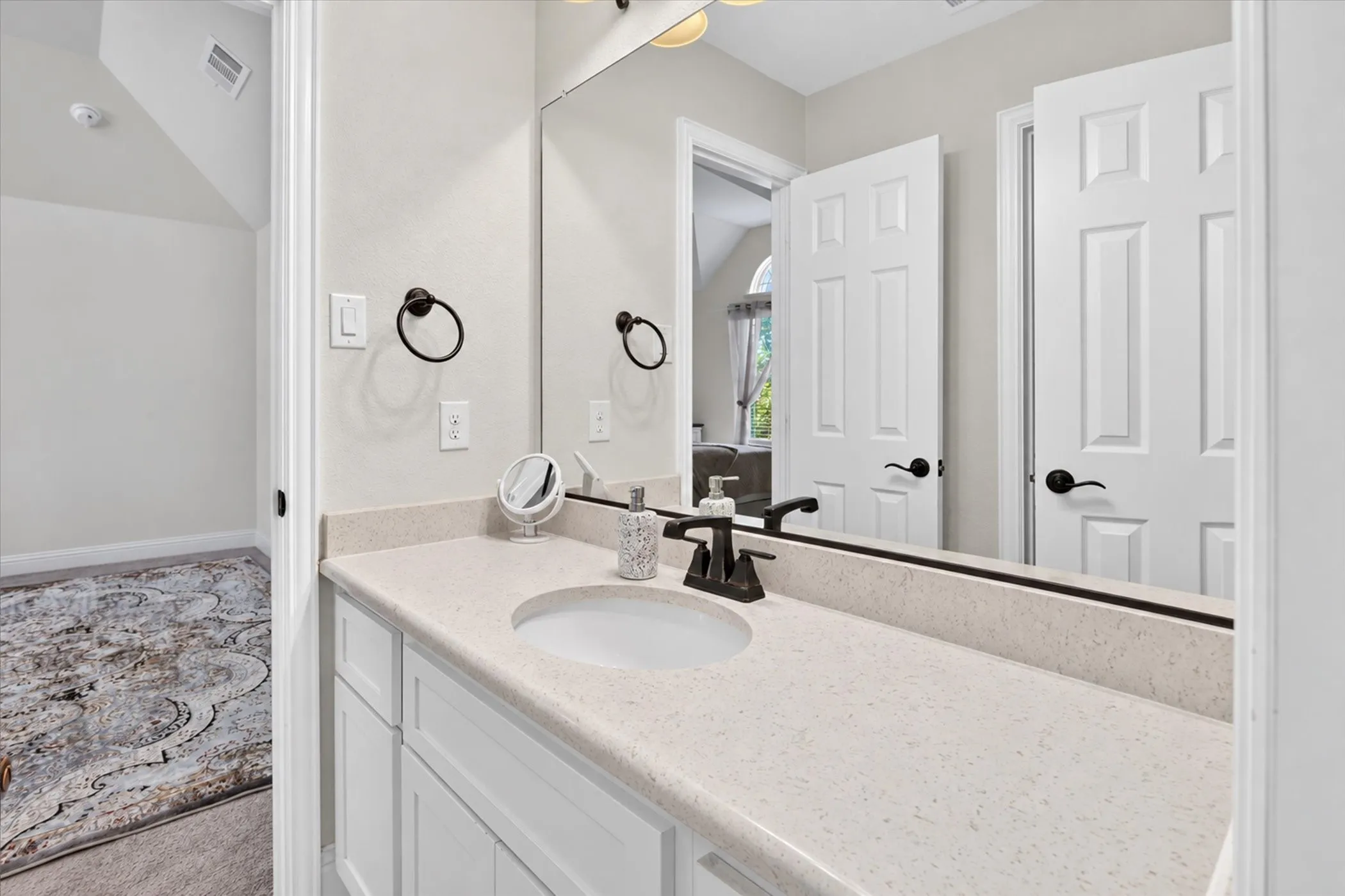 White vanity with an integrated sink, light-toned countertop, large wall mirror, and dark-finished faucet