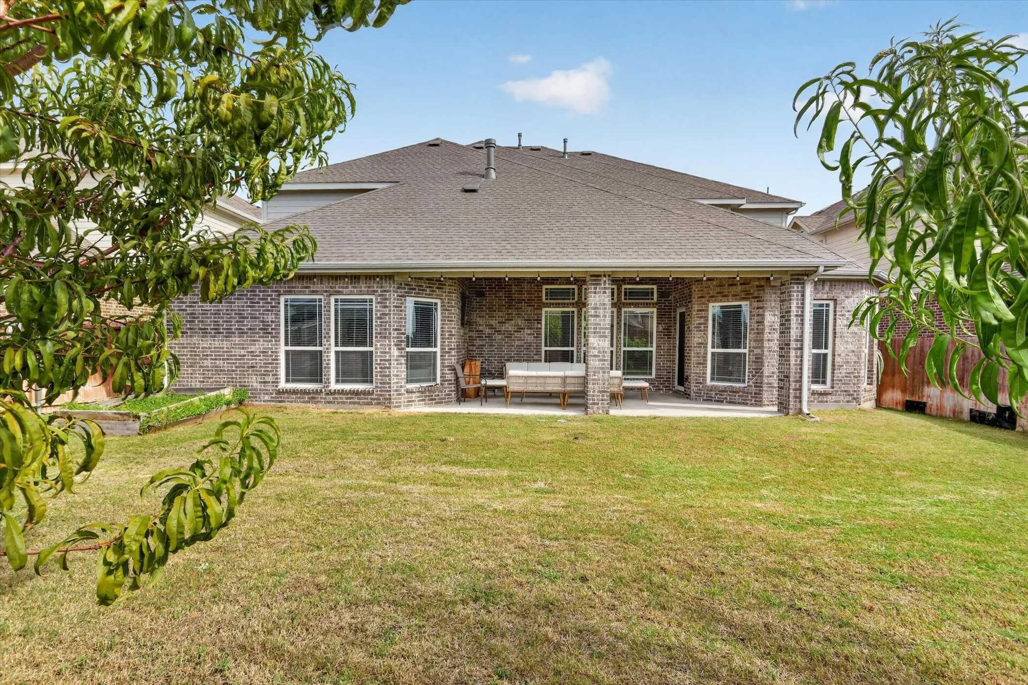 Expansive backyard featuring a covered patio, brick exterior, multiple windows, and a shingled roof