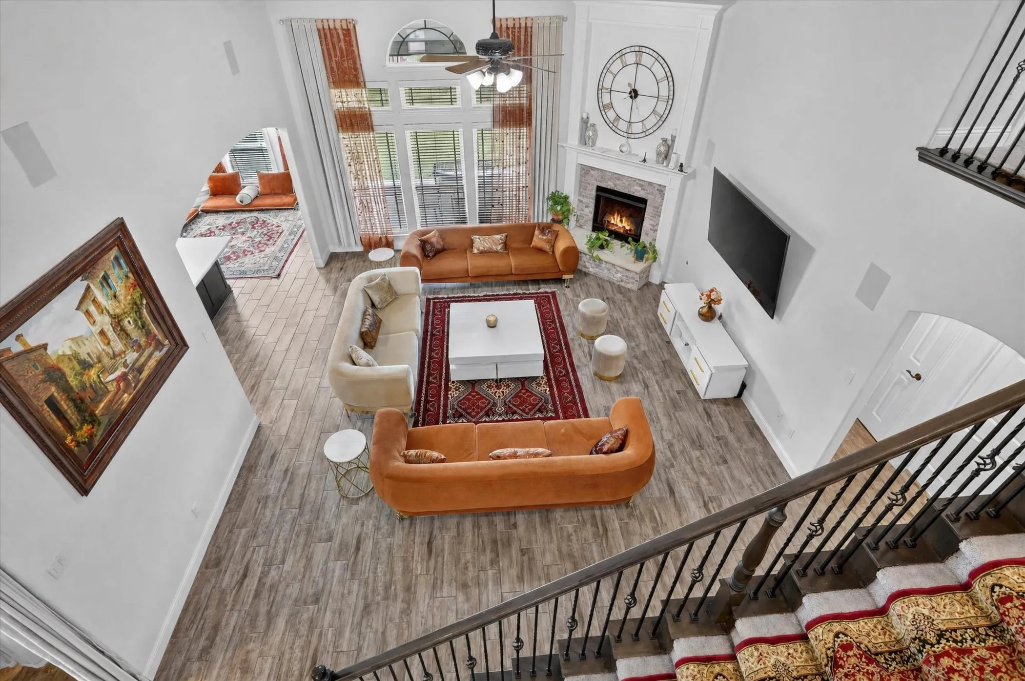 Two-story living area with wood-finish flooring, a stone fireplace, and an arched window