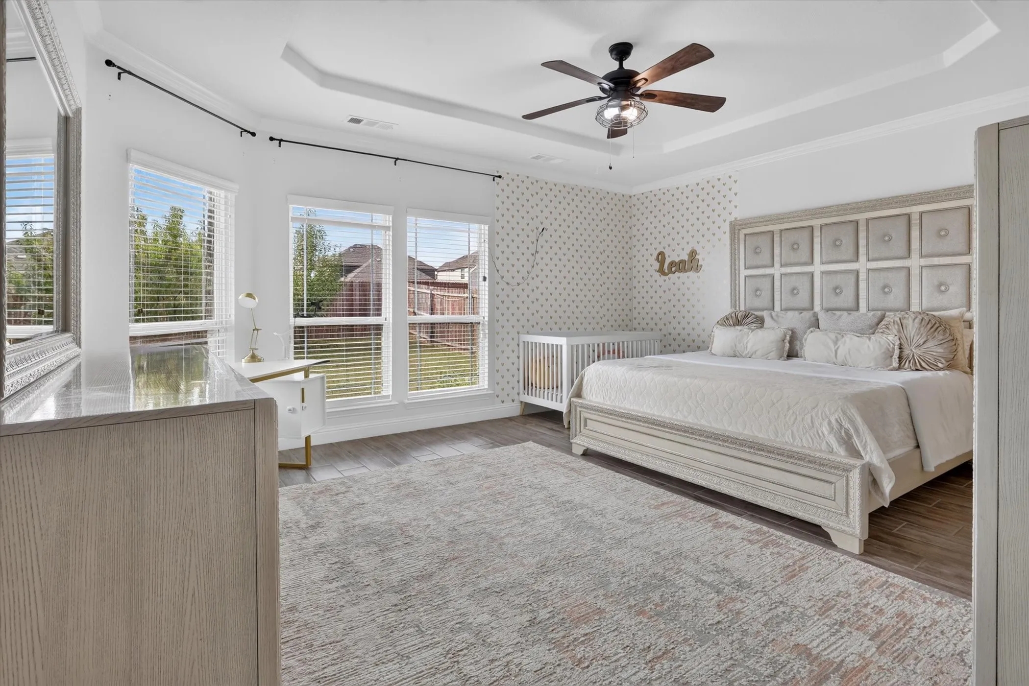 Tray ceiling with a ceiling fan, wood-finish flooring, and multiple windows providing natural illumination