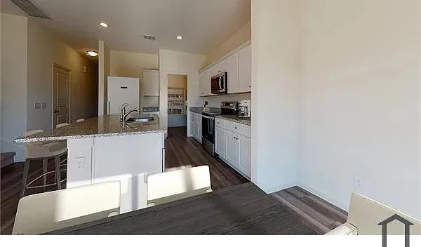 Kitchen featuring a large island with granite-style countertop, stainless steel appliances, white cabinetry, and wood-finish flooring