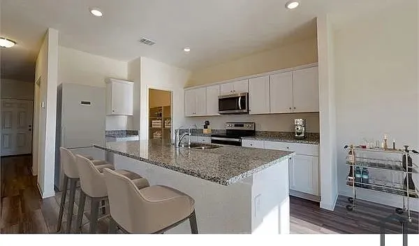 Kitchen featuring white cabinetry, granite countertops, stainless steel appliances, a center island with seating, and wood-finish flooring