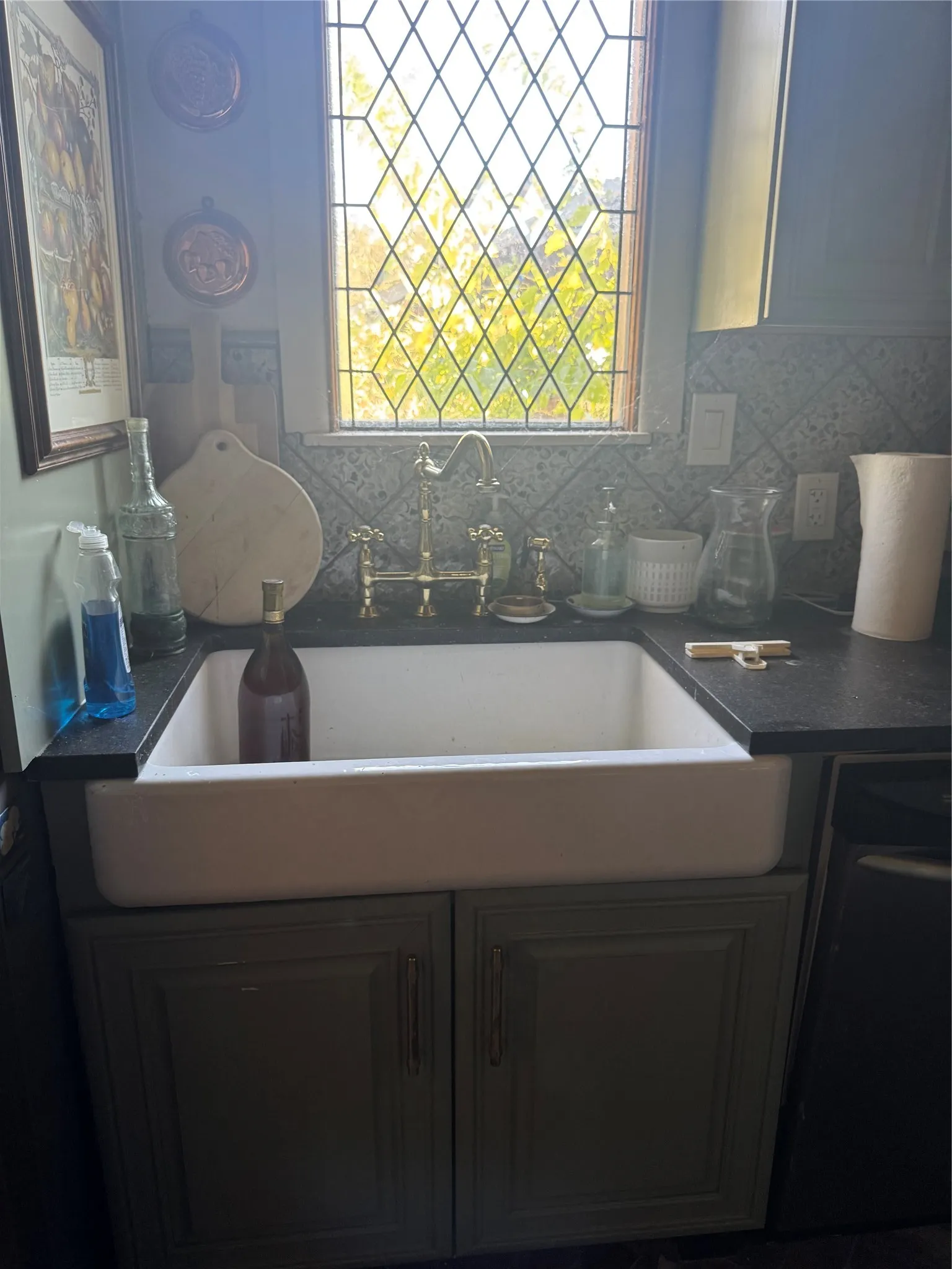 Farmhouse sink with a brass-finish faucet, dark countertops, and a patterned tile backsplash