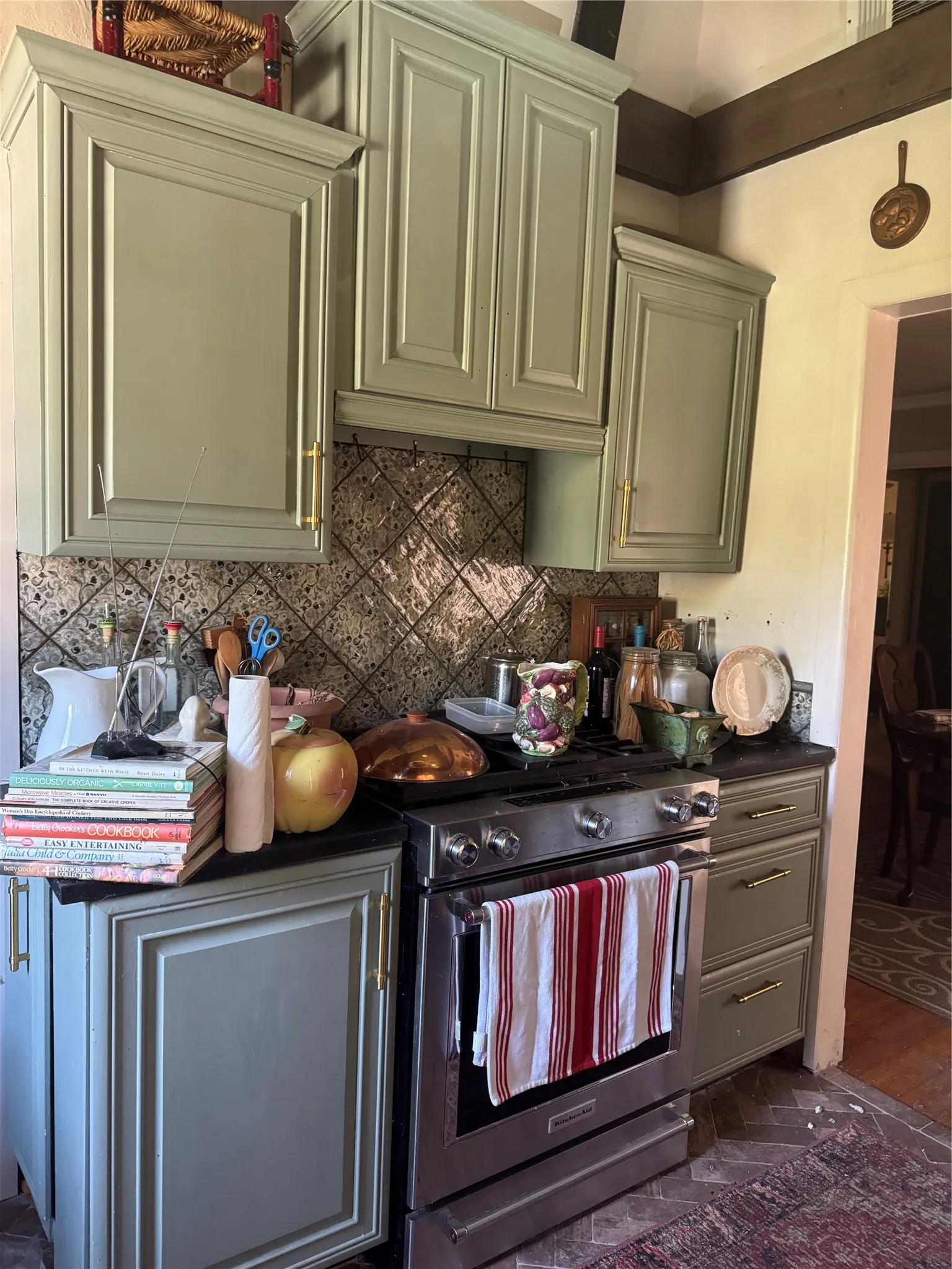 Sage-painted cabinetry with brass hardware, black countertops, stainless steel range, and a decorative tile backsplash