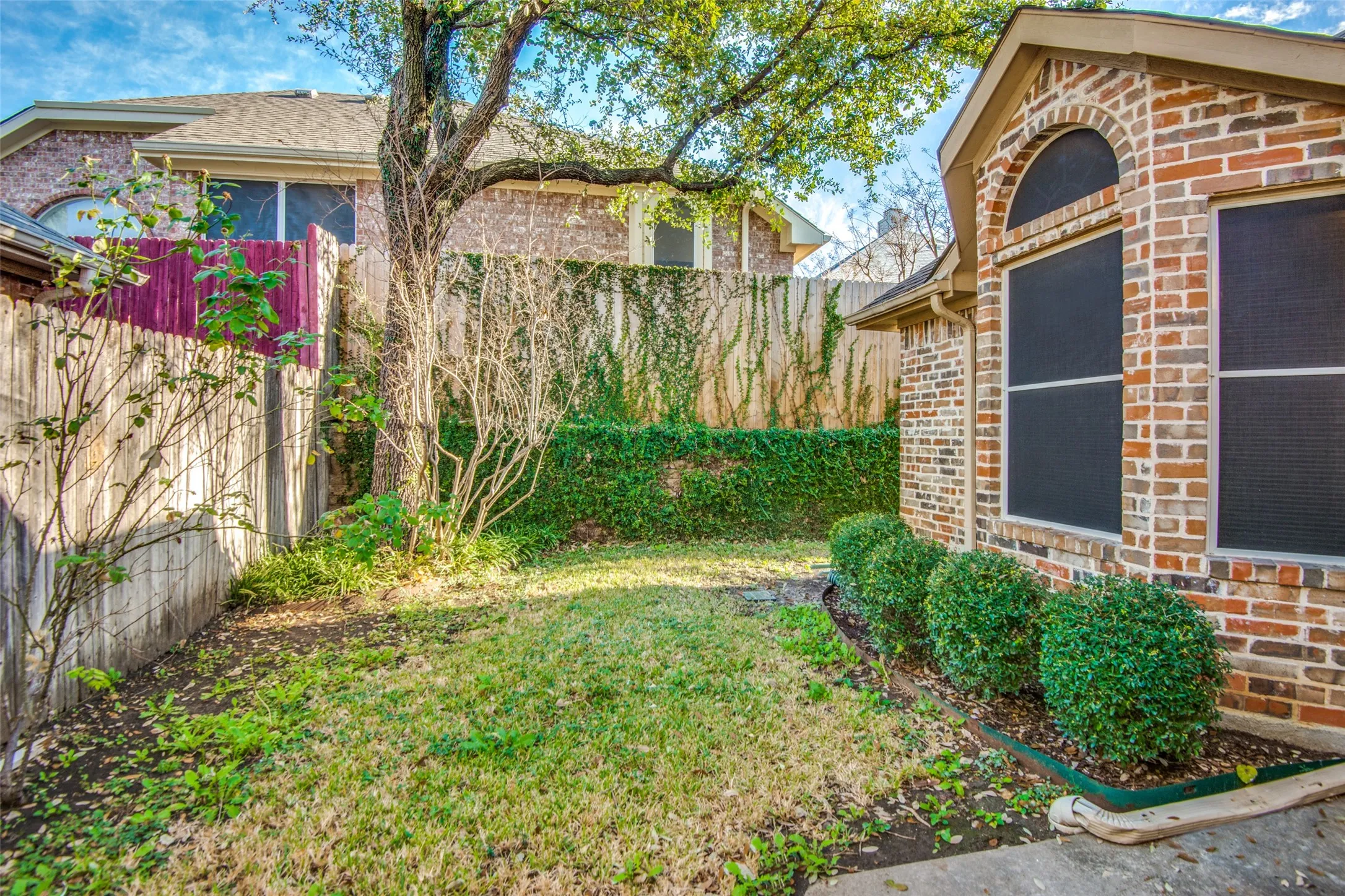 Brick exterior with an arched window, featuring a manicured shrub bed and a grassy yard