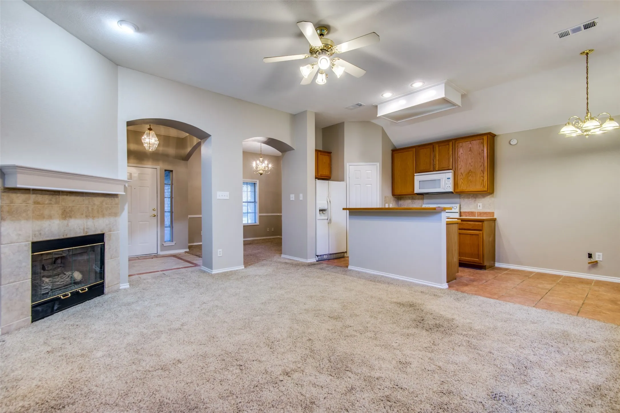 Tiled fireplace surround with mantel, arched doorways, kitchen with wood cabinetry, white appliances, and a breakfast bar, and vaulted ceilings with a ceiling fan