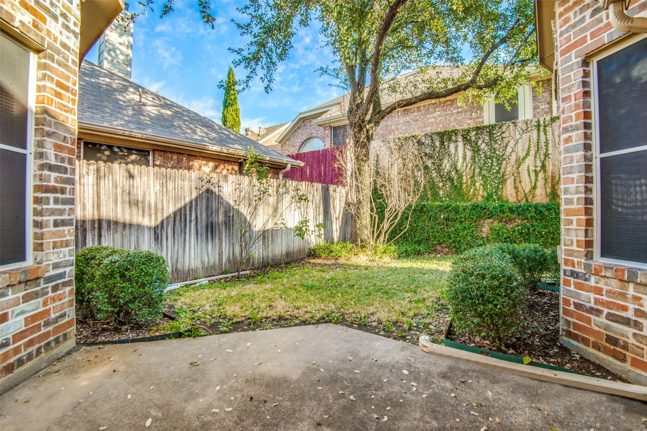 Private outdoor patio with a concrete surface, bordered by brick exterior walls and a wooden fence