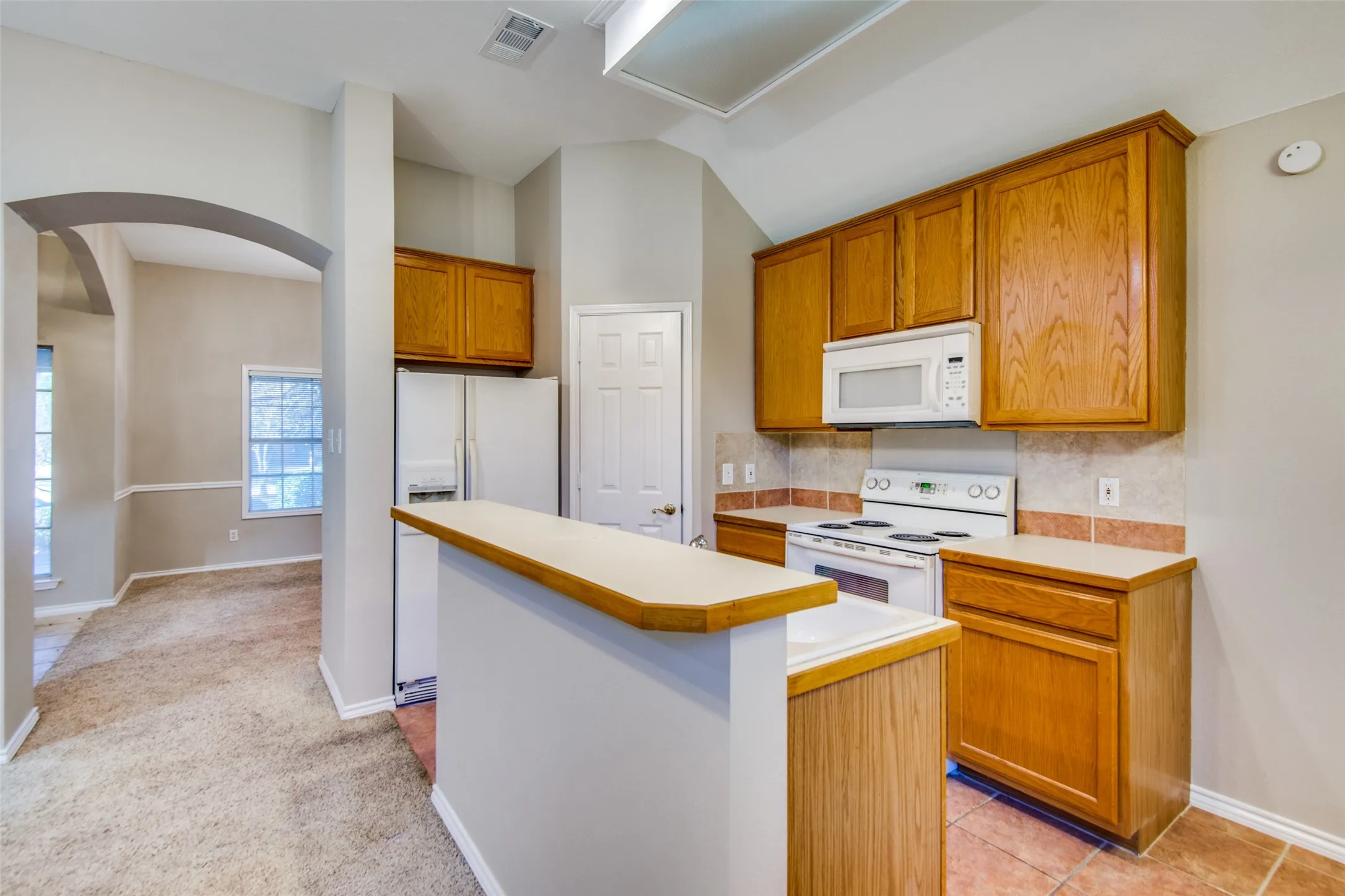 Kitchen featuring wood cabinetry, white appliances, and a breakfast bar