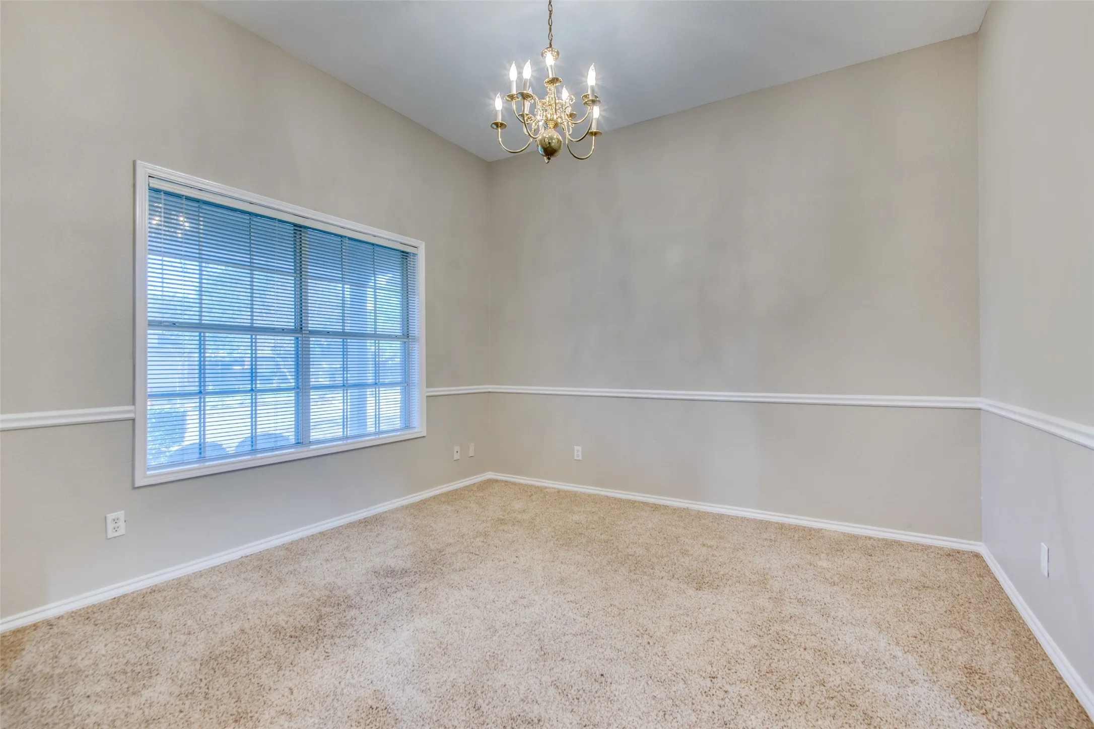 Vaulted ceiling, decorative chandelier, large window with blinds, chair rail molding, and carpeting