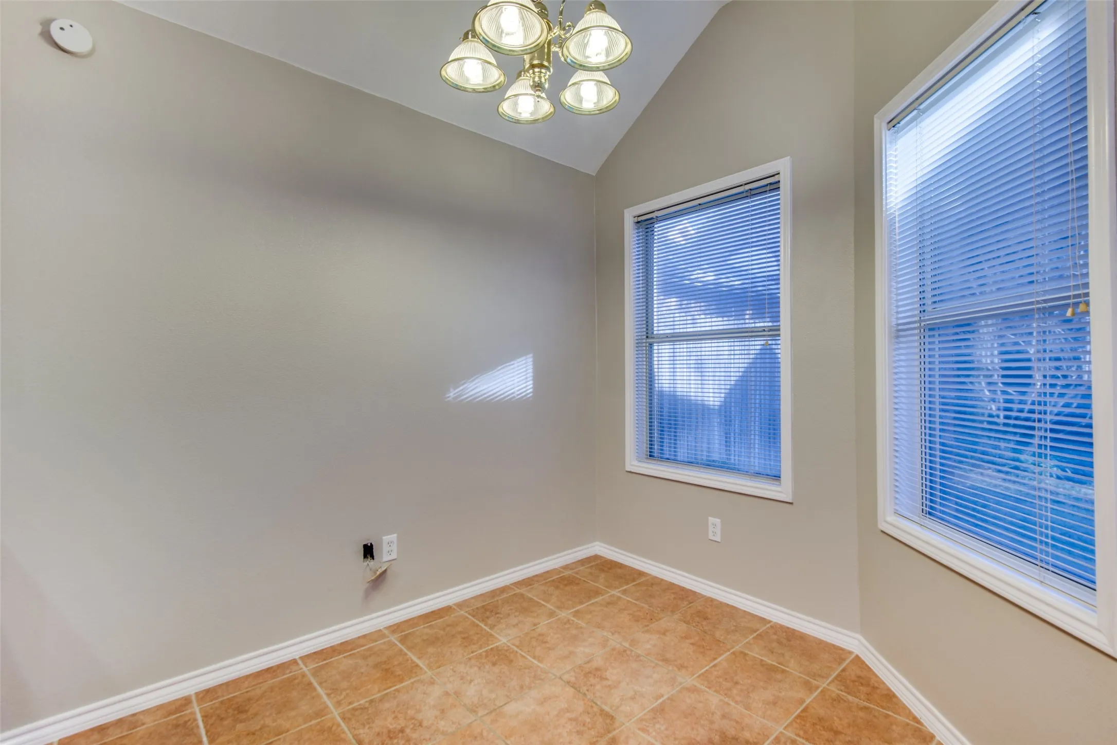 Angled ceiling with a five-light chandelier, two windows with blinds, and tile flooring