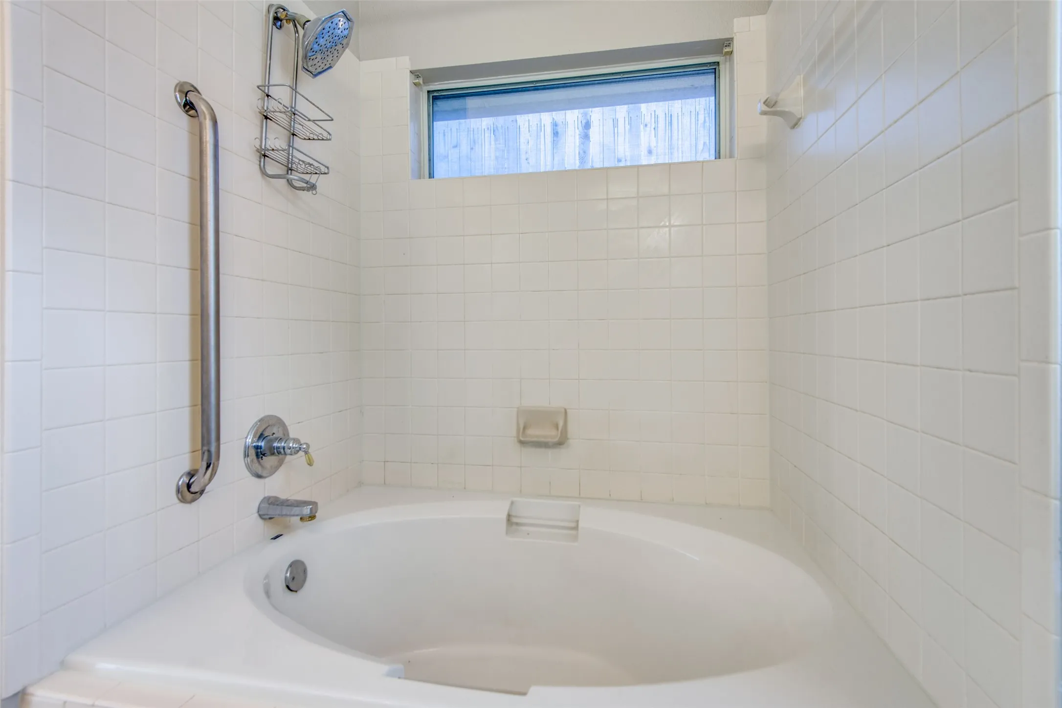 Built-in soaking tub with chrome fixtures, white subway tile surround, and an integrated grab bar