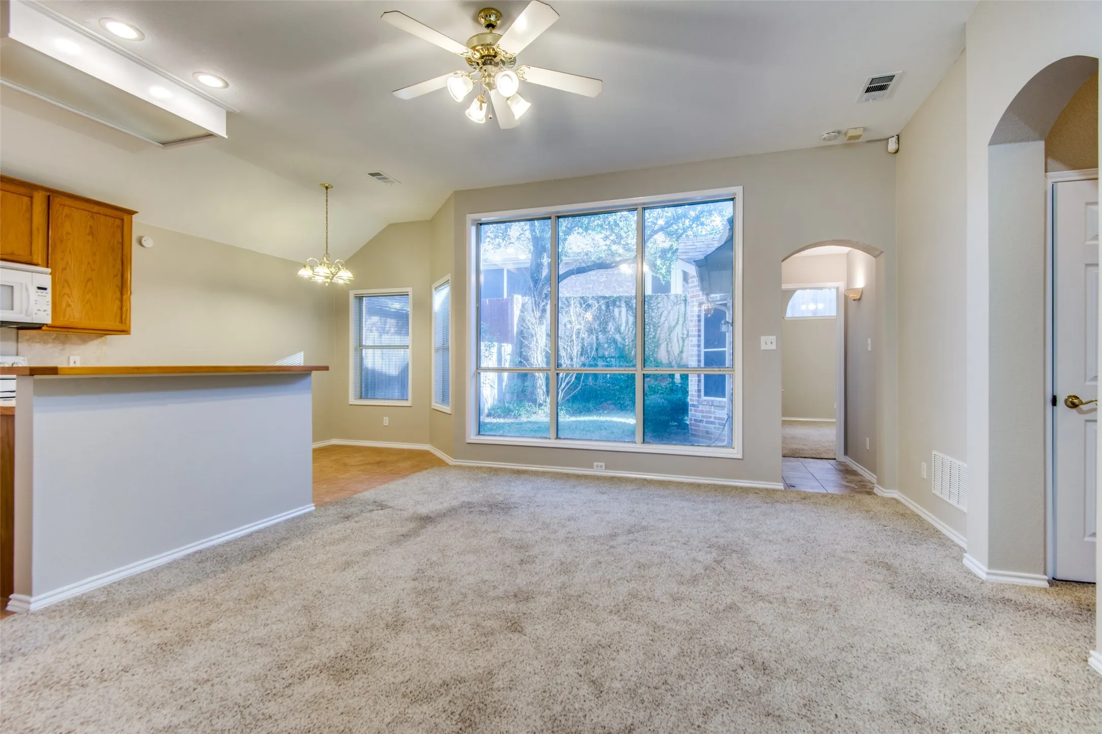 Vaulted ceilings, large picture windows, arched doorways, ceiling fan, and built-in kitchen cabinetry
