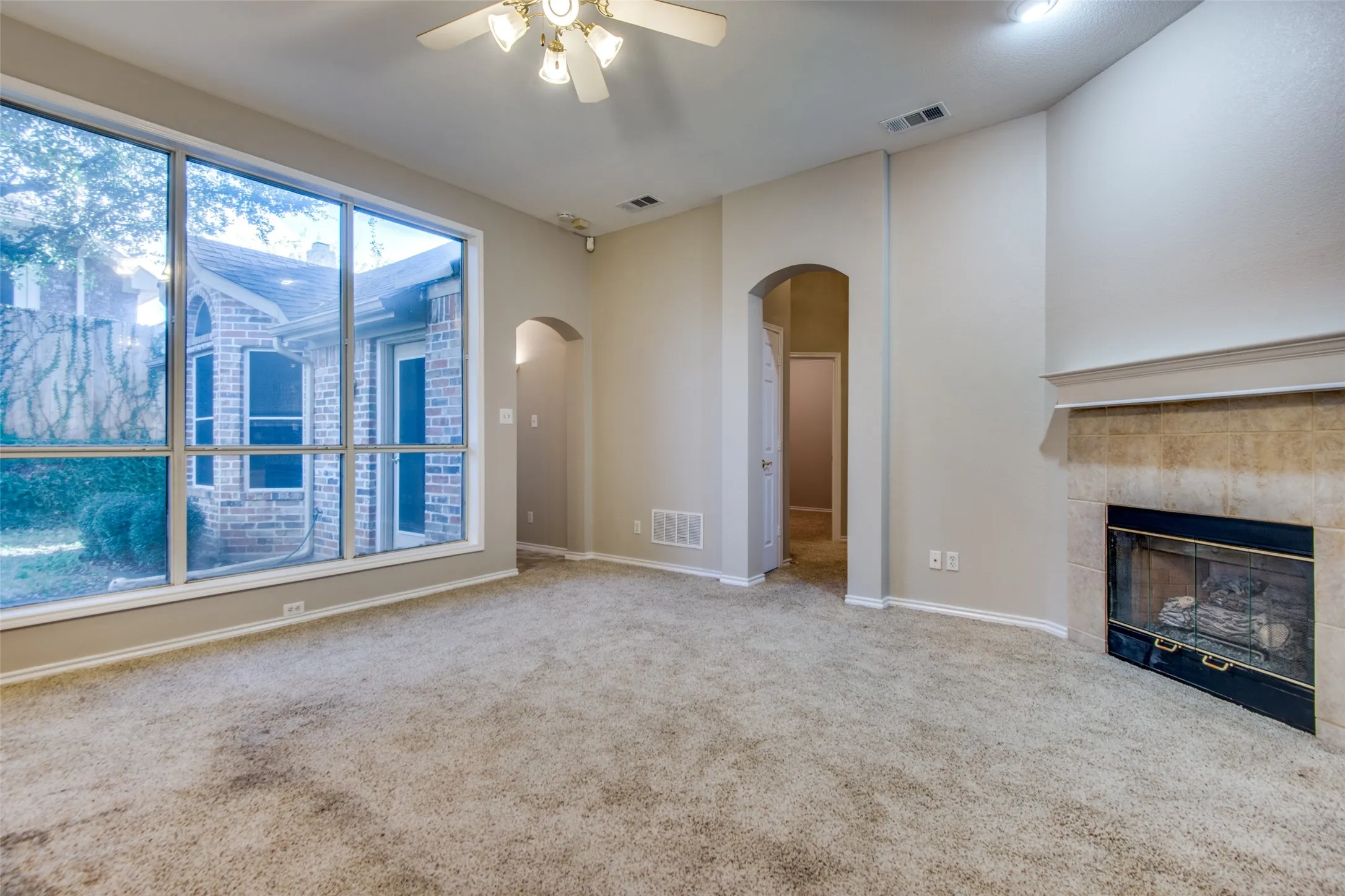 Expansive windows, arched doorways, ceiling fan, and a fireplace with a stone surround