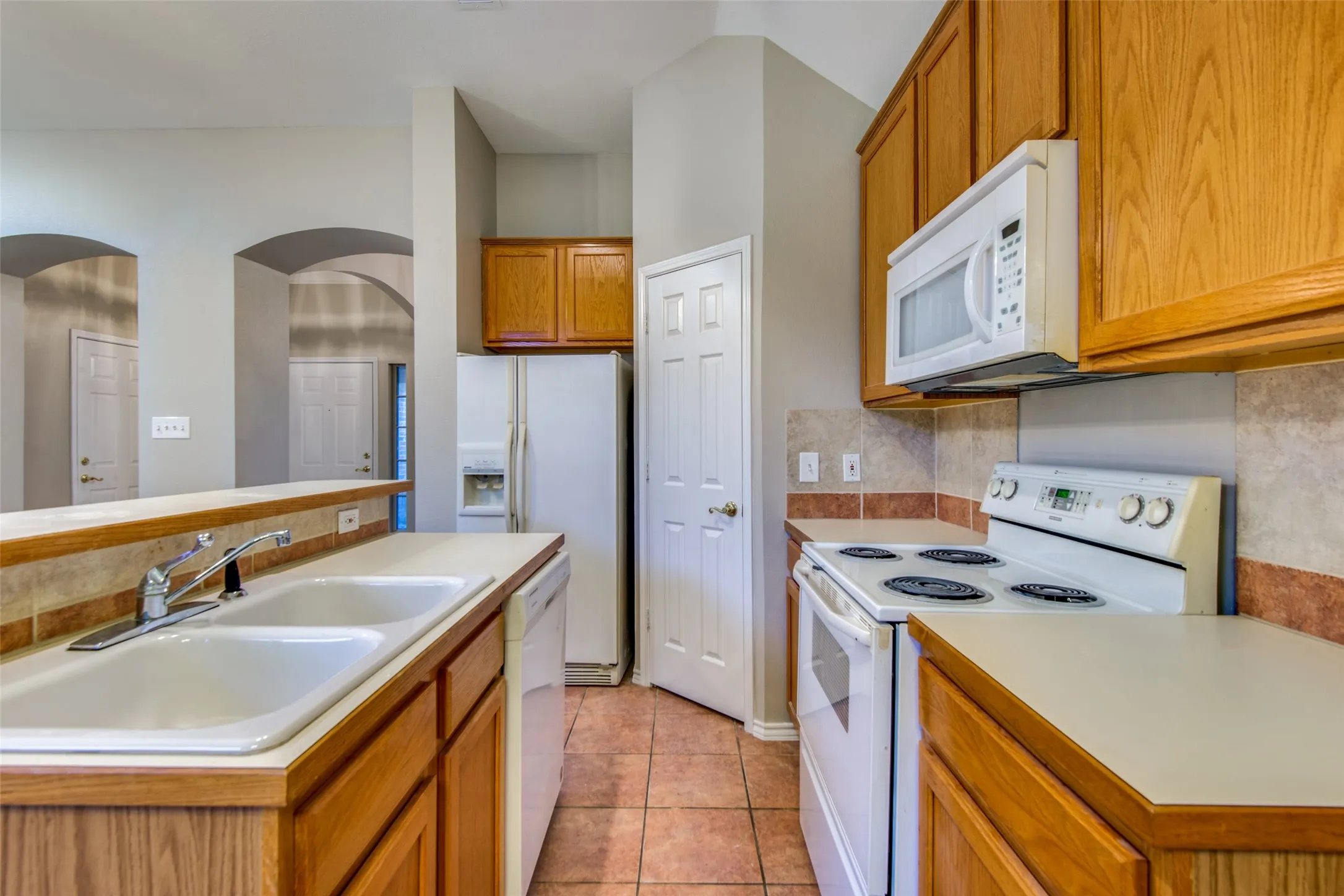 Kitchen featuring wood-finish cabinetry, tile flooring, and integrated white appliances
