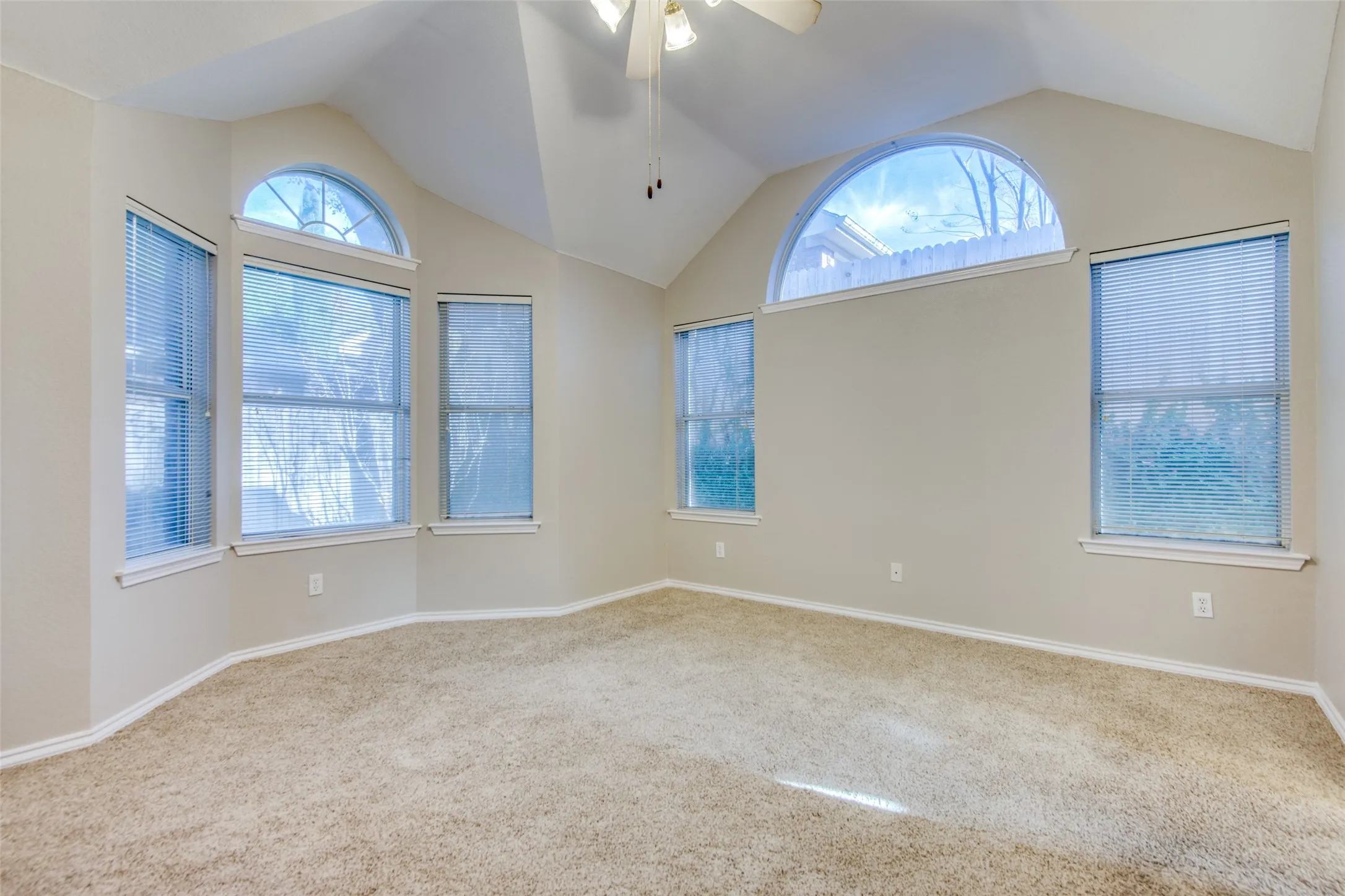 Vaulted ceilings, arched windows, multiple windows, neutral-toned carpet, ceiling fan
