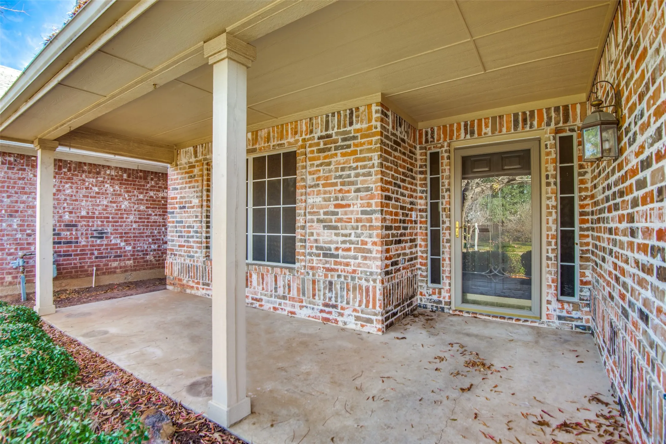 Covered front entry featuring a brick facade, decorative columns, and a porch light