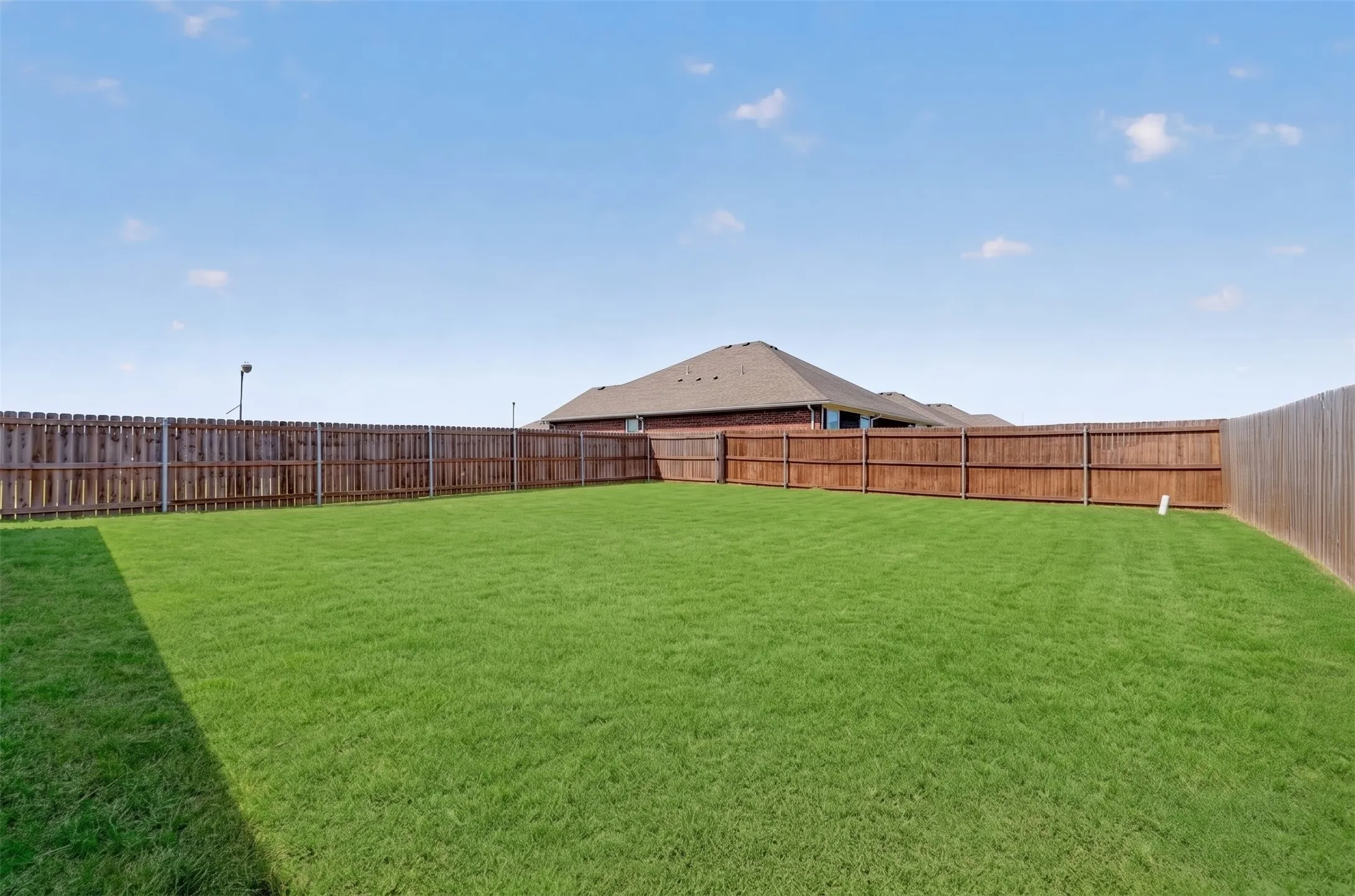 Expansive backyard featuring a lush lawn and perimeter wood fencing