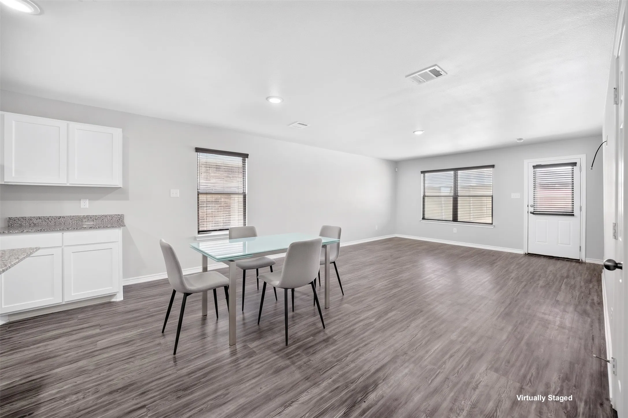 Open-concept living space featuring wood-finish flooring, recessed lighting, white cabinetry, granite-style countertops, and multiple windows