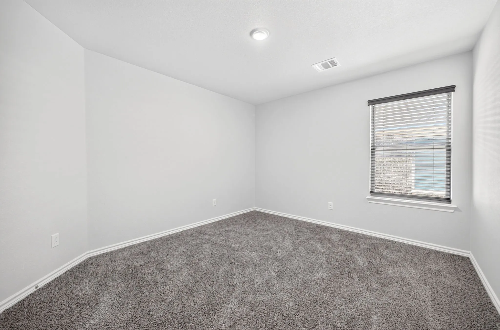 Neutral-toned walls, recessed ceiling lighting, textured gray carpeting, and a window with blinds