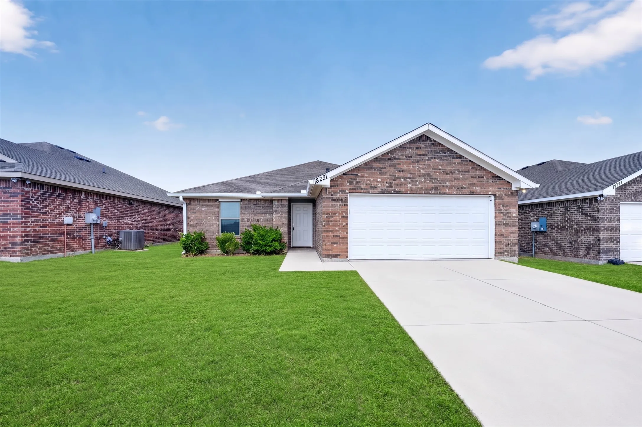 Brick exterior with an attached garage, paved driveway, front lawn, and mature landscaping