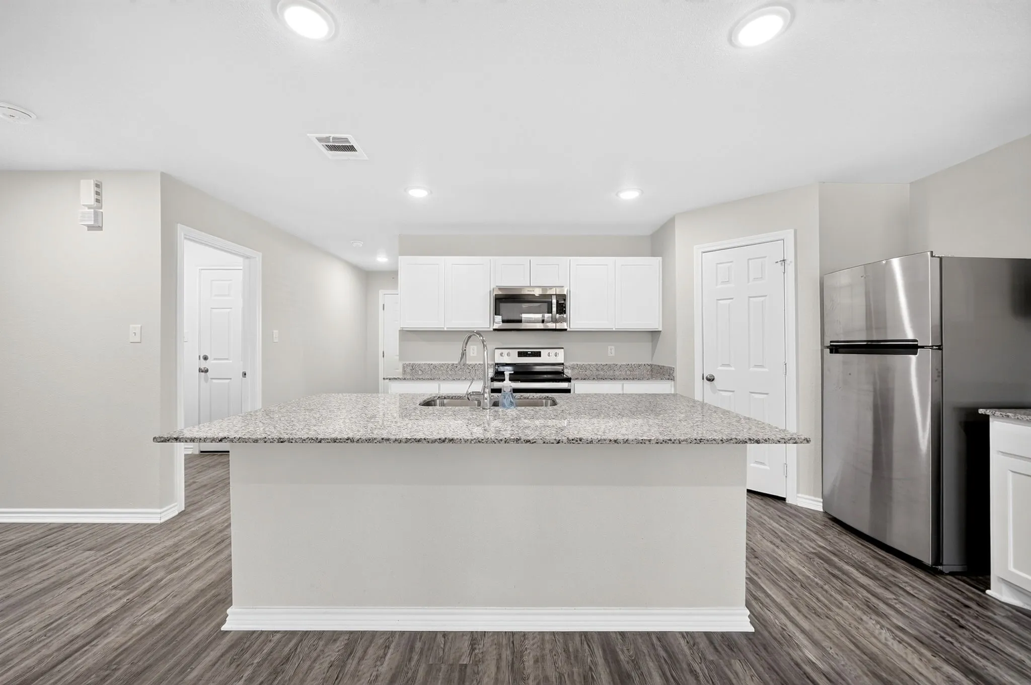 Kitchen featuring a central island with an undermount sink, white cabinetry, integrated stainless steel appliances, and wood-finish flooring