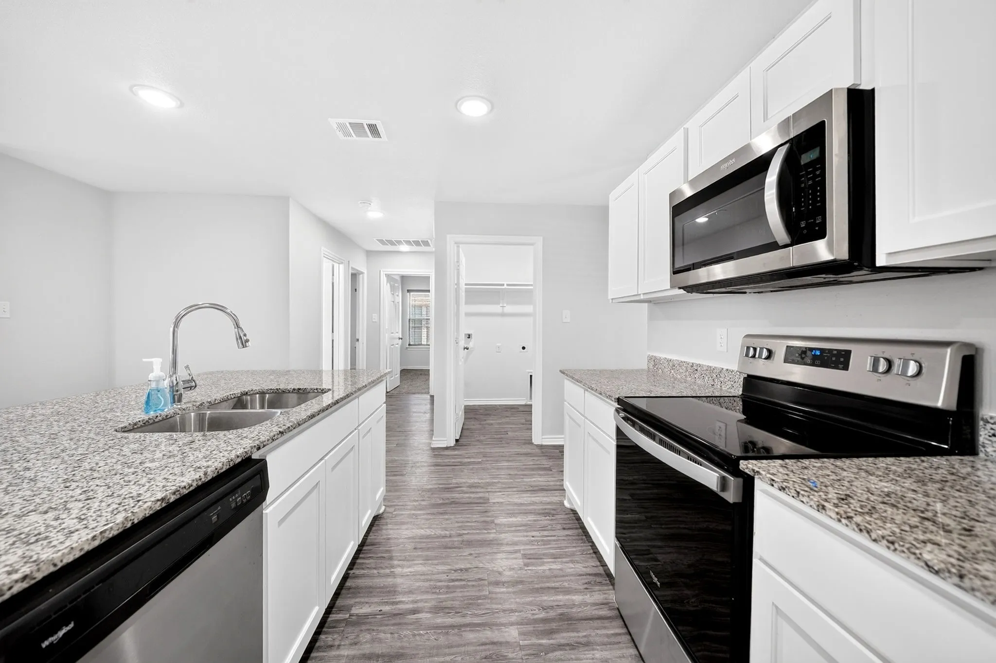 Kitchen featuring granite countertops, wood-finish flooring, white cabinetry, stainless steel appliances, and recessed lighting