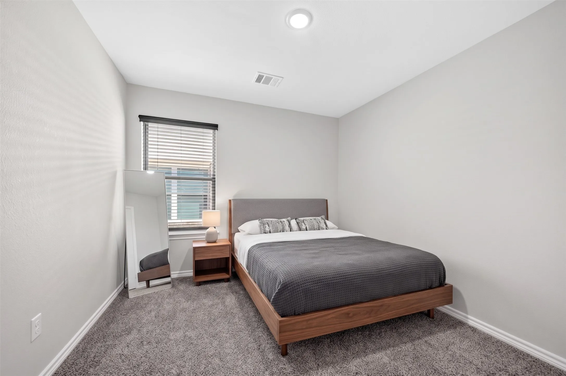 Light grey wall finish, recessed ceiling lighting, textured carpet flooring, and a window with blinds