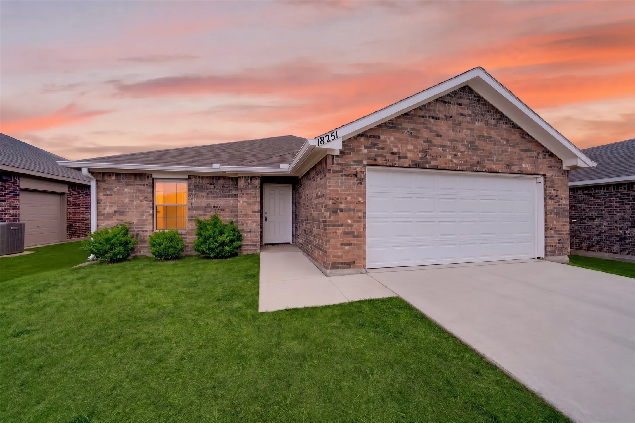 Brick exterior with white trim, attached two-car garage, concrete driveway, and a well-maintained lawn