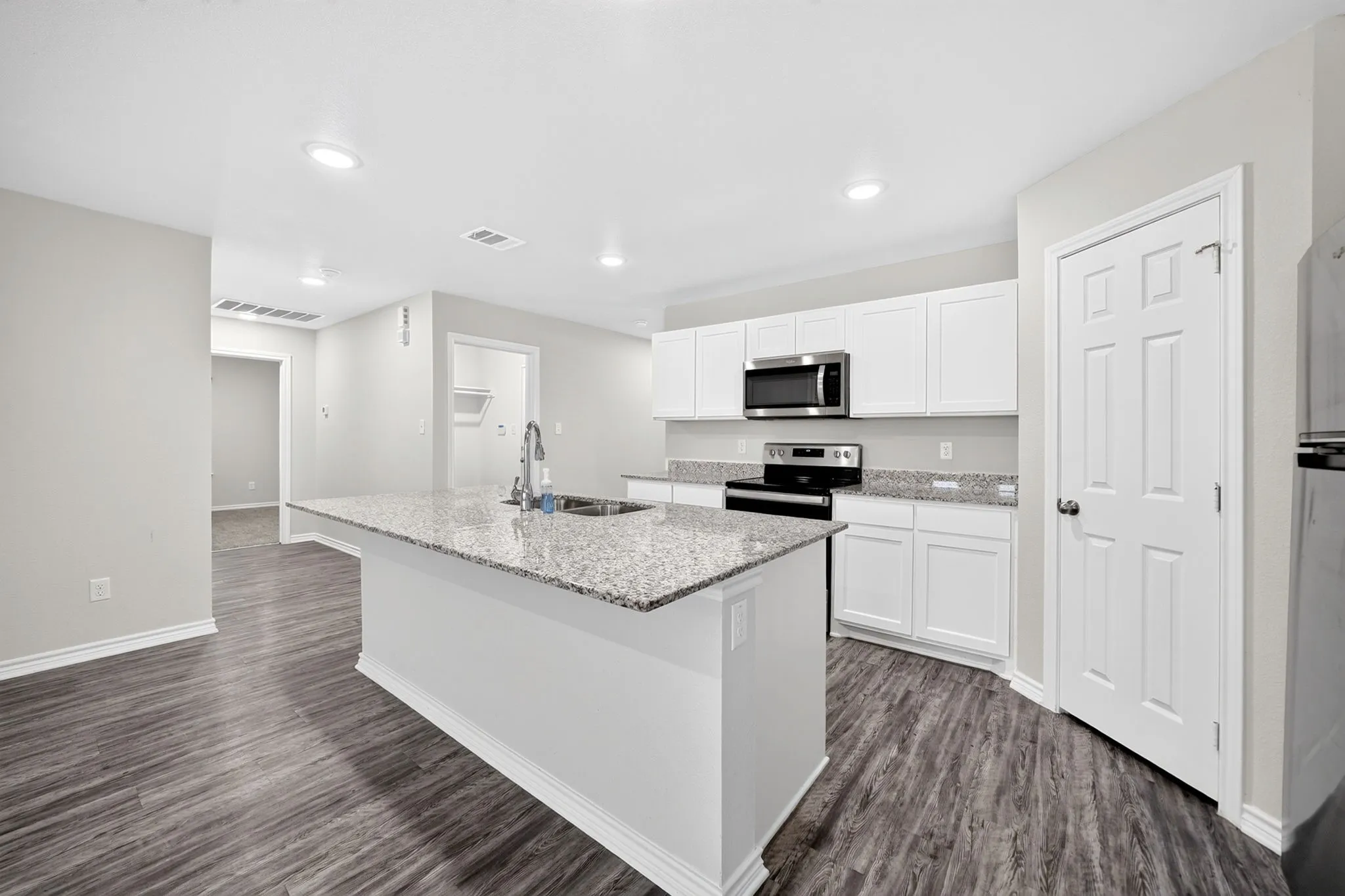 Kitchen island with an undermount sink, granite countertops, wood-finish flooring, white cabinetry, and stainless steel appliances
