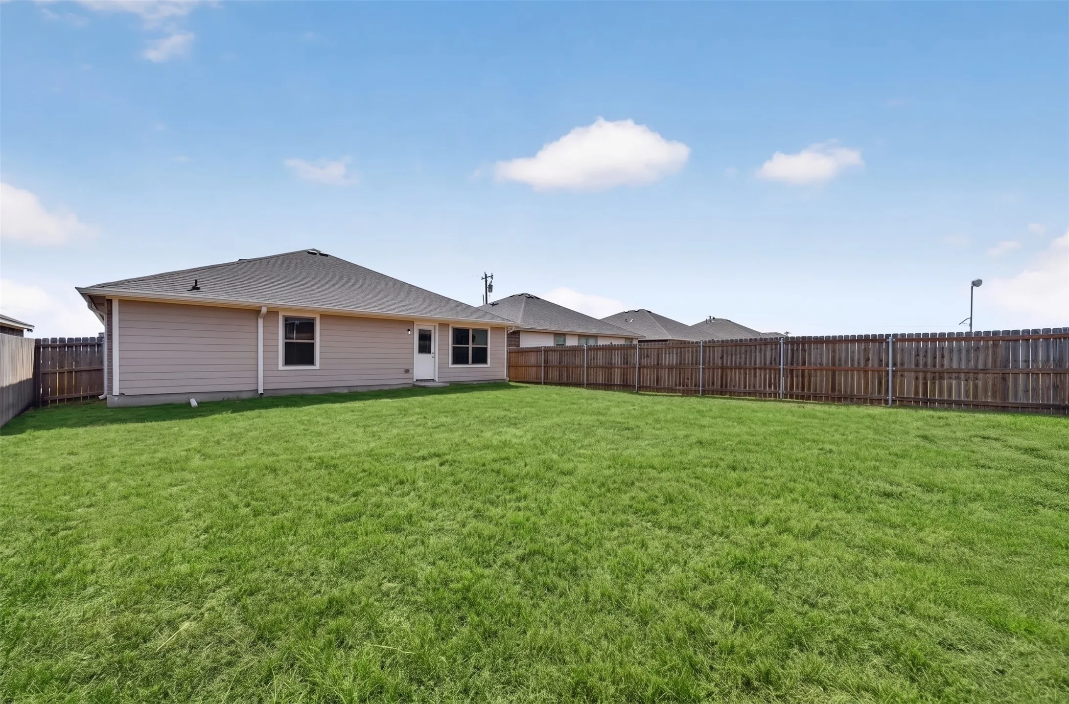 Expansive backyard featuring a manicured lawn, full perimeter privacy fencing, and a single-story residence with a gabled roof