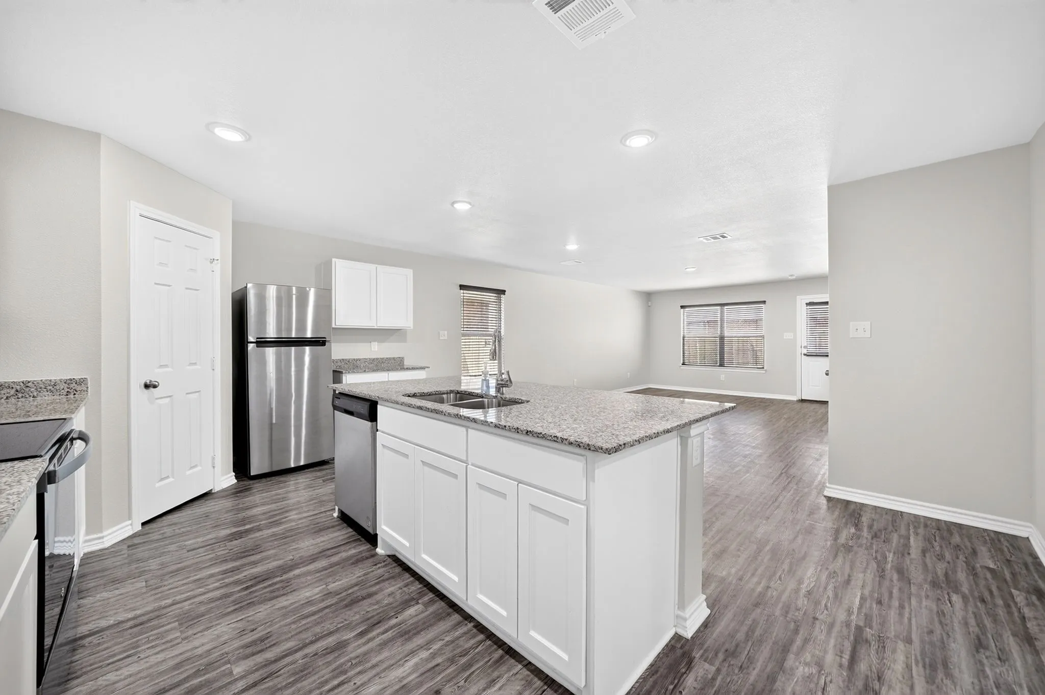 Kitchen island with granite countertop, stainless steel appliances, white cabinetry, recessed lighting, and wood-finish flooring