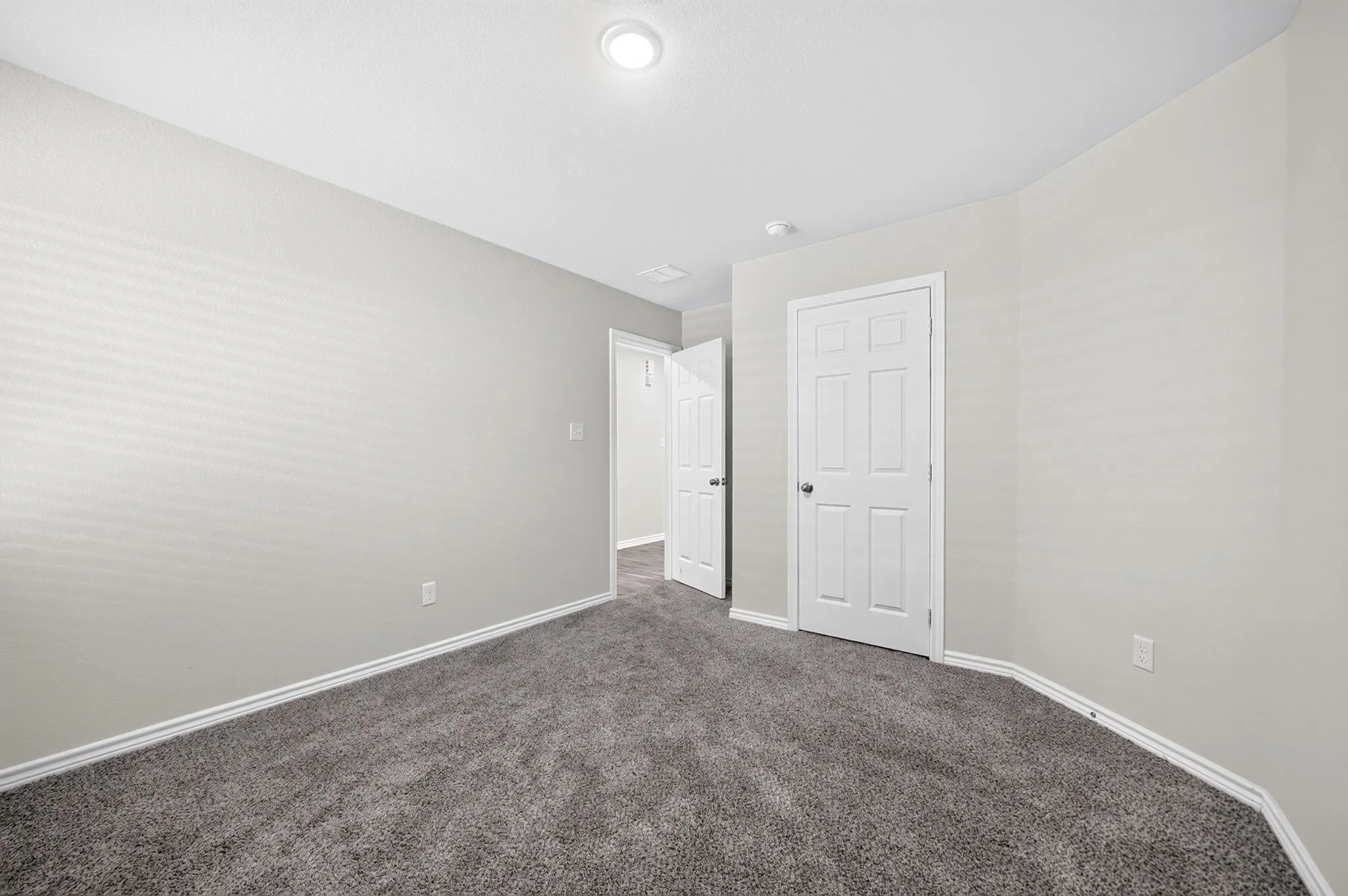 Neutral wall paint, gray carpeting, a six-panel door, and recessed lighting