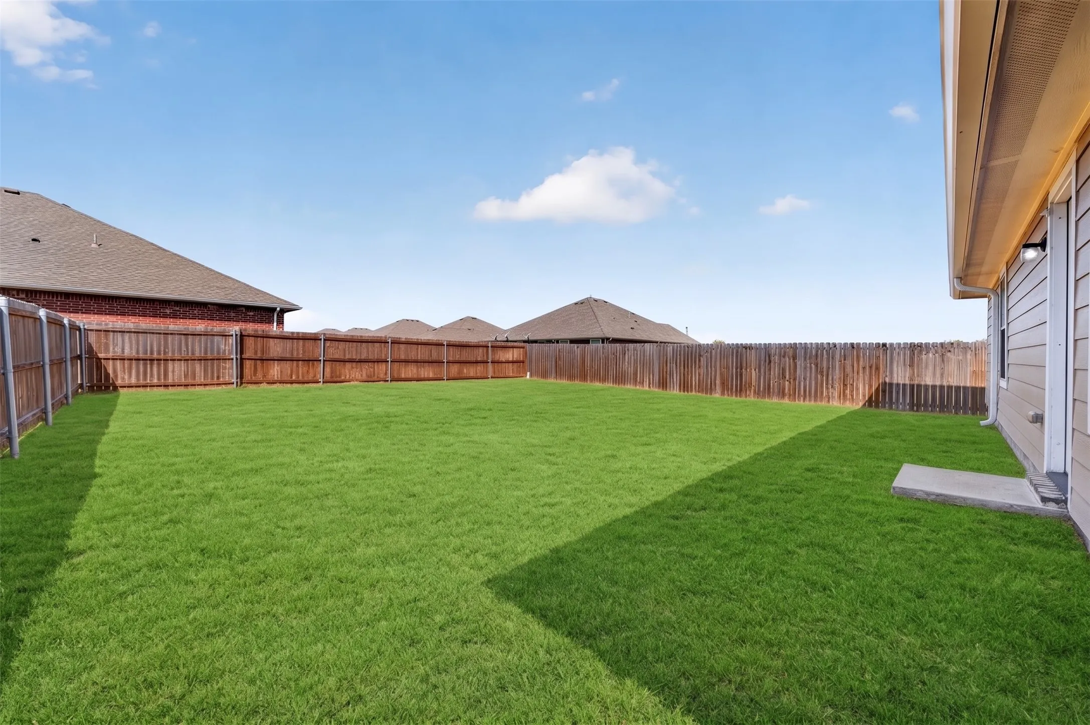 Expansive backyard featuring a manicured lawn, full wood privacy fencing, and a concrete patio pad