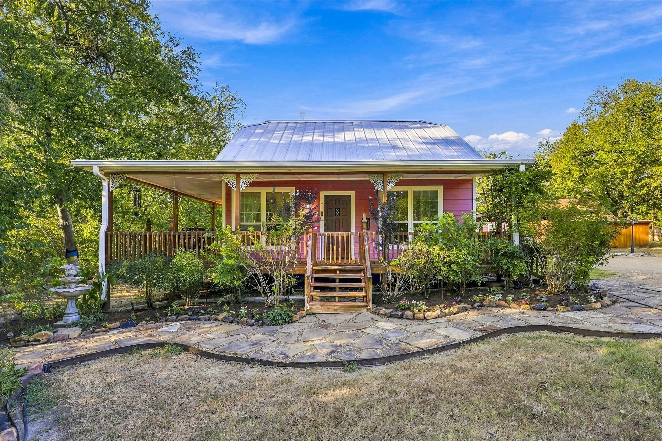Exterior featuring a covered front porch, a metal roof, a stone walkway, and mature landscaping