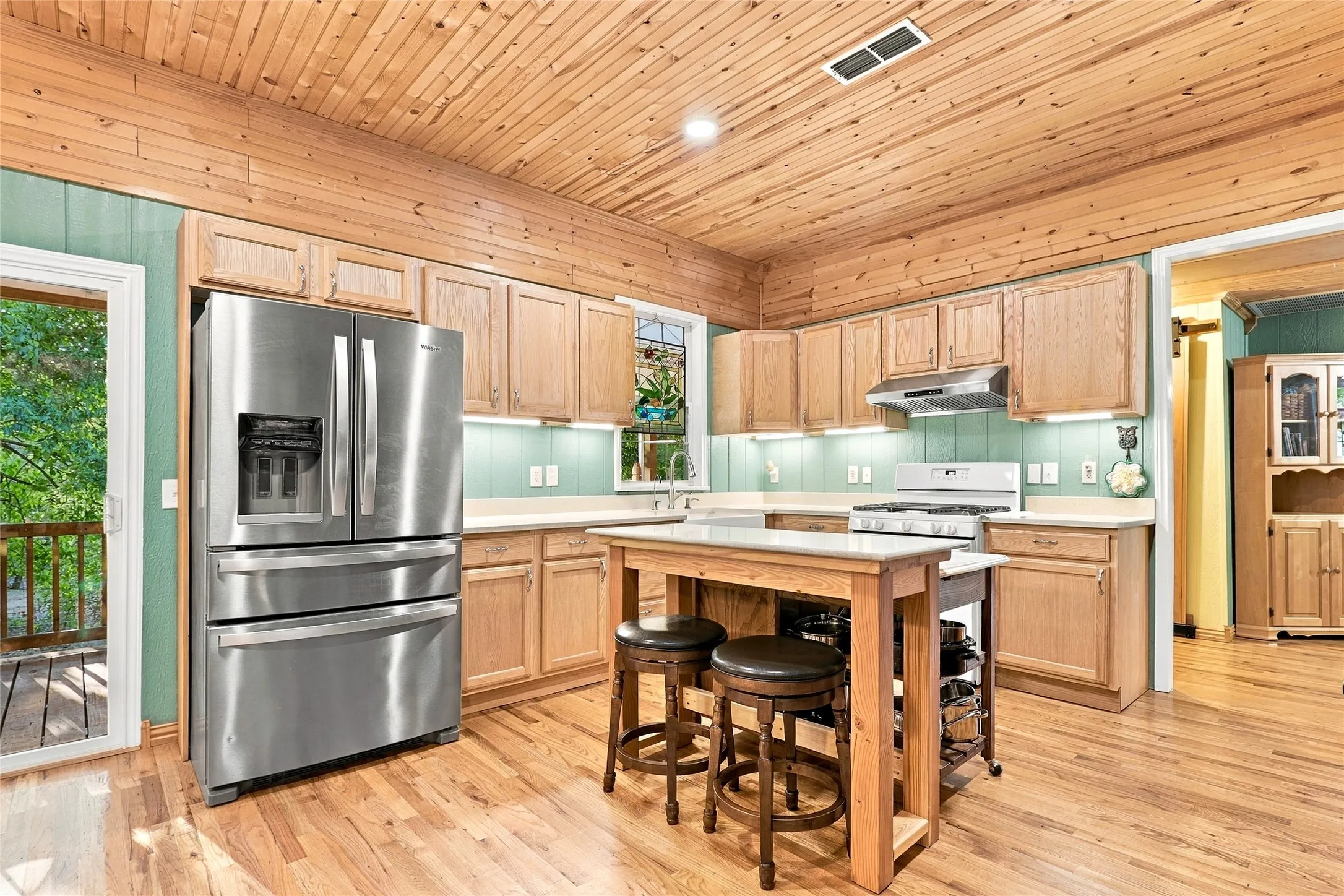 Wood-finish plank ceiling, wood-finish flooring, stainless steel refrigerator, wood-finish cabinetry, and a kitchen island