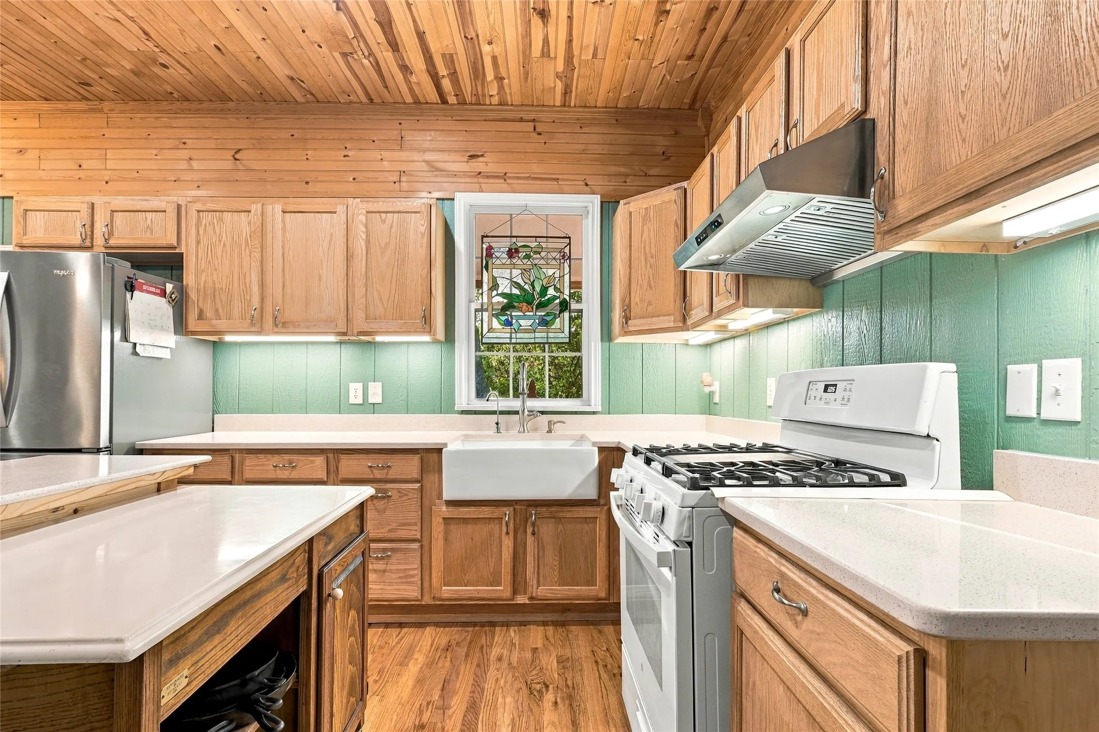 Kitchen featuring wood-finish flooring, wood-paneled ceiling, light wood cabinetry, white countertops, and a white farmhouse sink