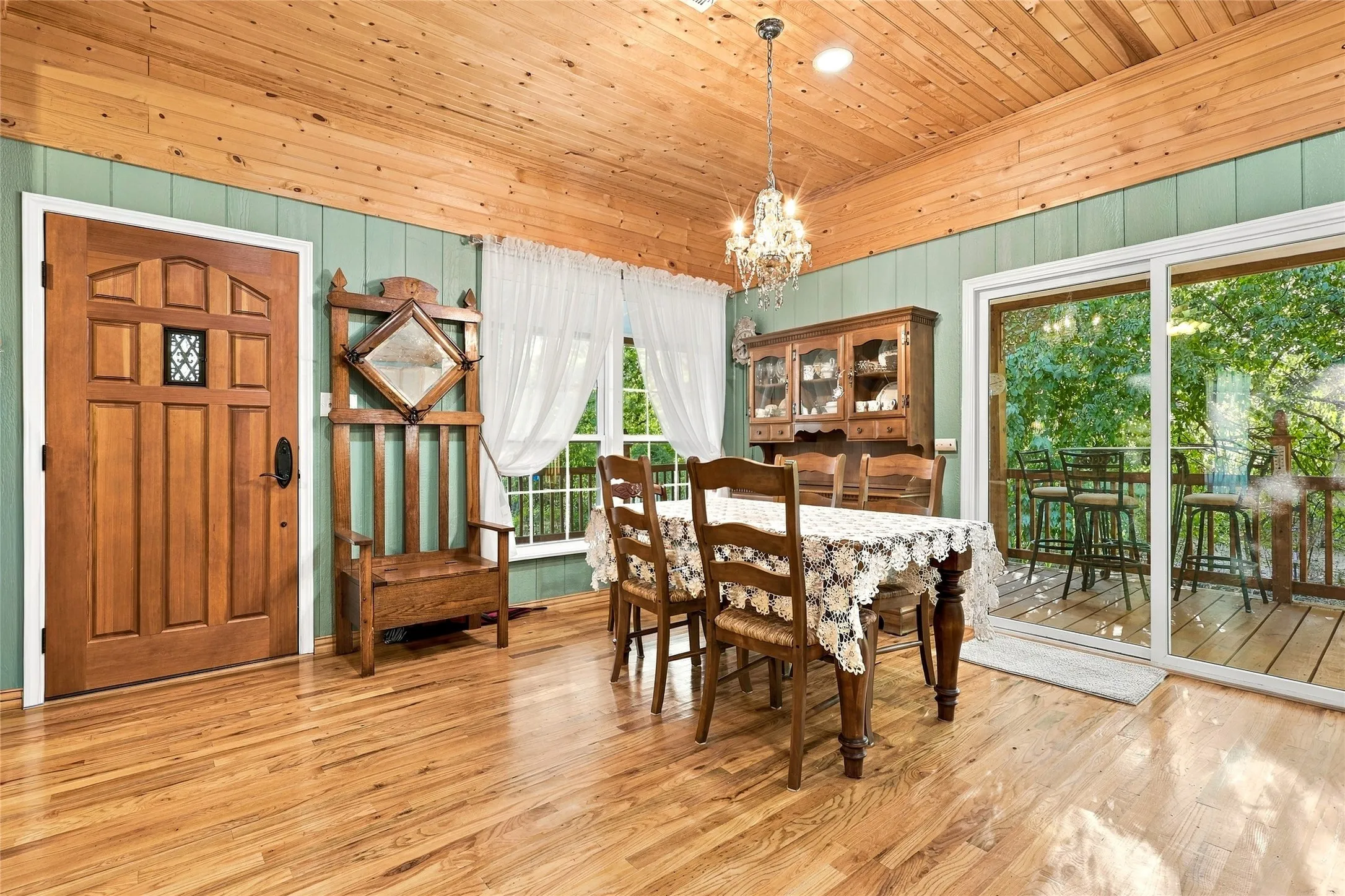 Wood-finish flooring, wood plank ceiling, paneled accent wall, sliding glass door, and a crystal chandelier