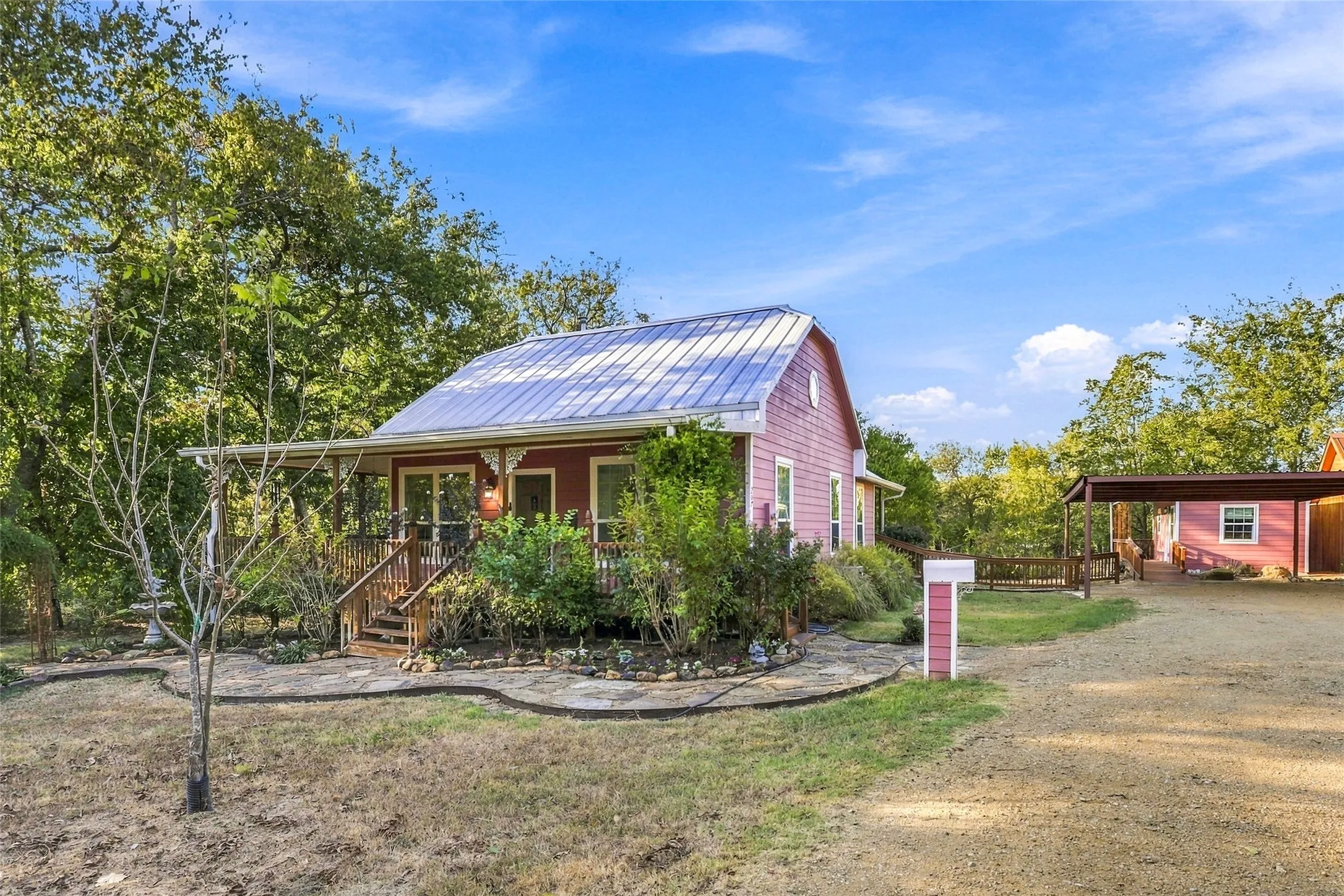 Red-sided residence featuring a metal roof, front porch with wood railings, and a gravel driveway