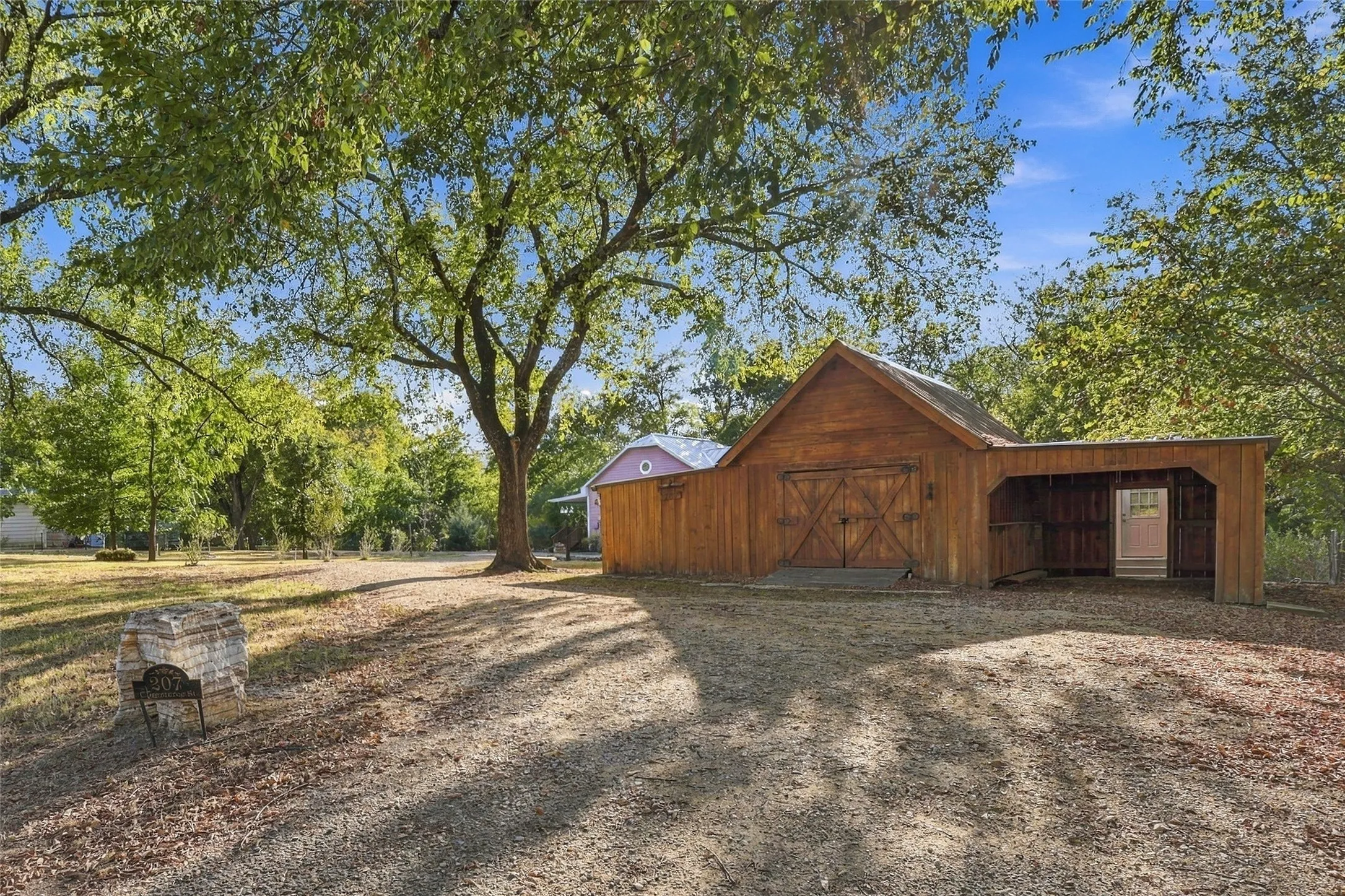 Wood-sided barn with gabled roof, dual barn doors, and an attached covered lean-to structure