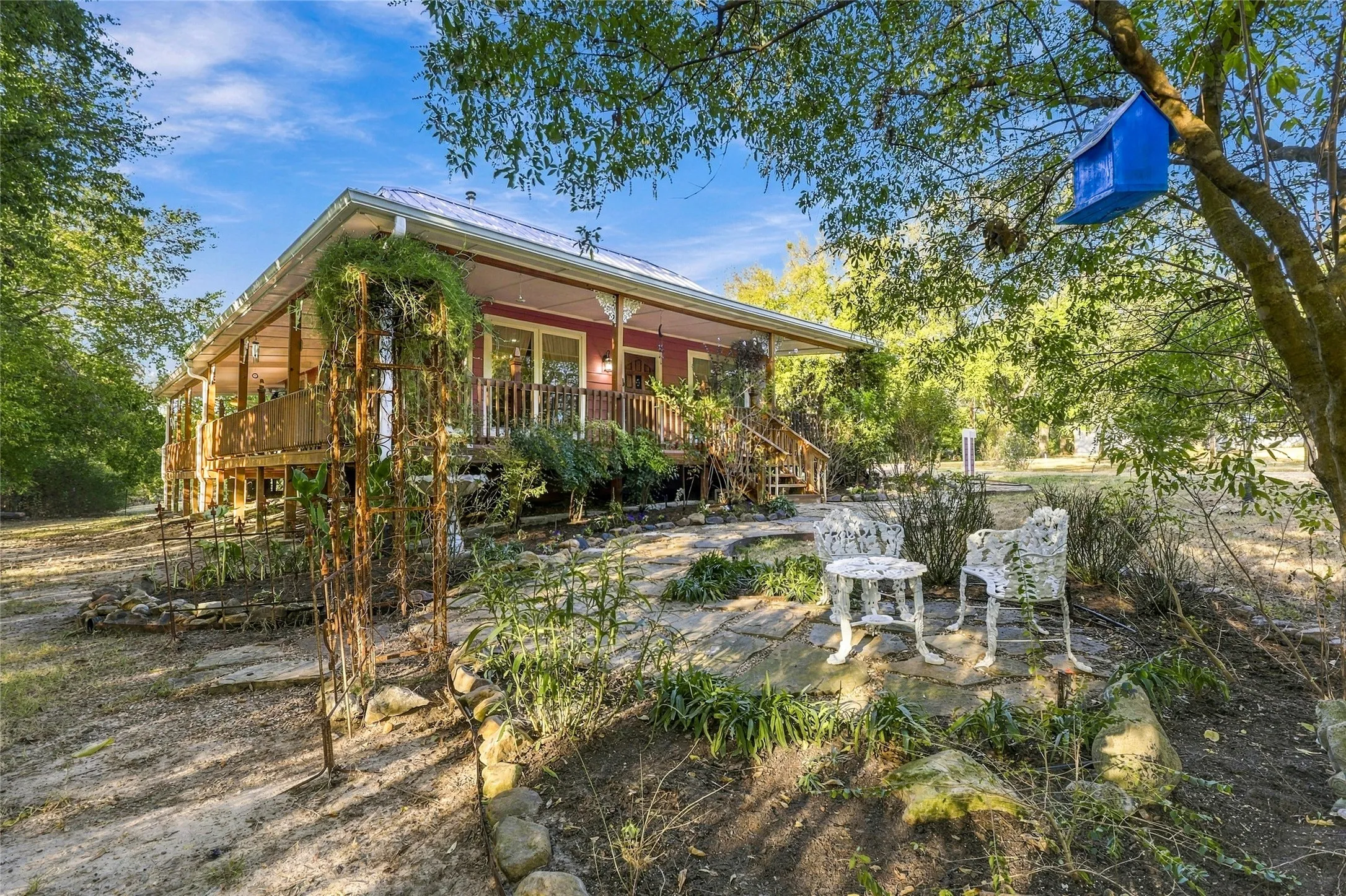 Elevated home with a covered front porch, red siding, wood railings, and a white metal roof
