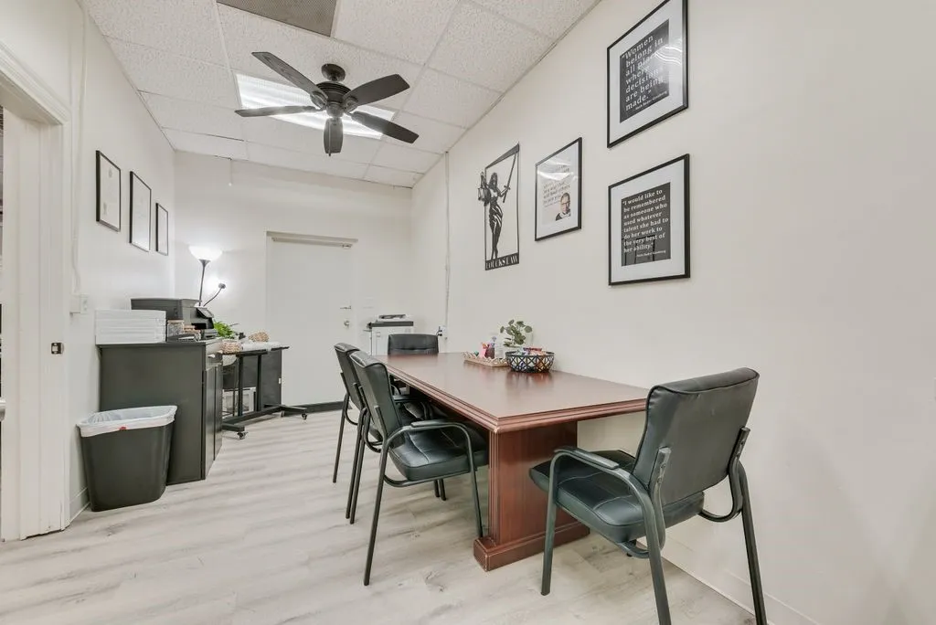 Wood-finish flooring, drop ceiling with recessed lighting, ceiling fan, white painted walls, and a door with a lever handle